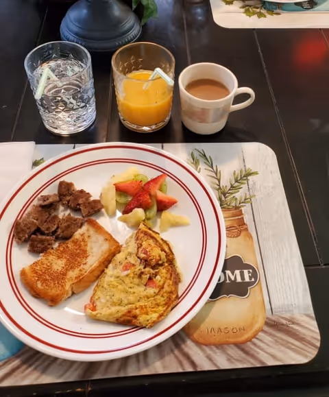 Plate with toast, omelette, fruit, orange juice, coffee, and water on a dining table.