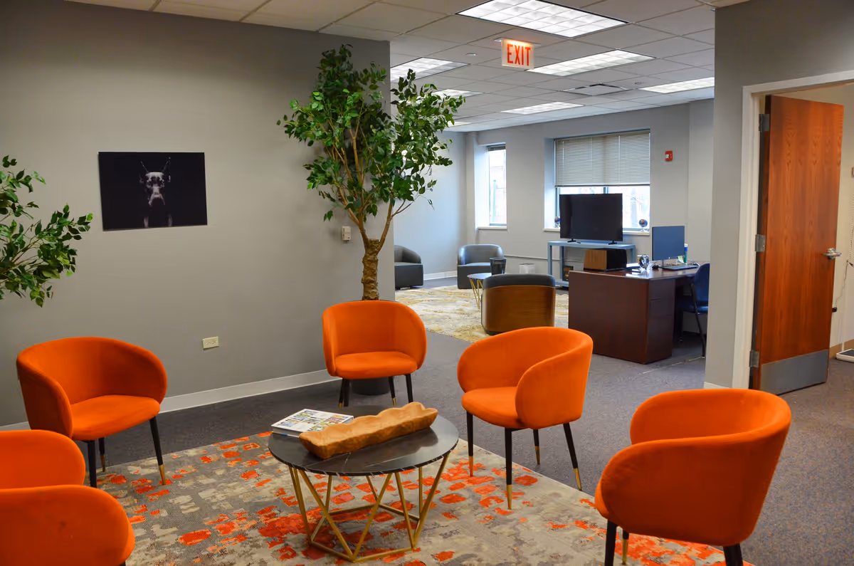 A modern lounge with orange chairs, plants, and a desk in a quiet senior living facility.