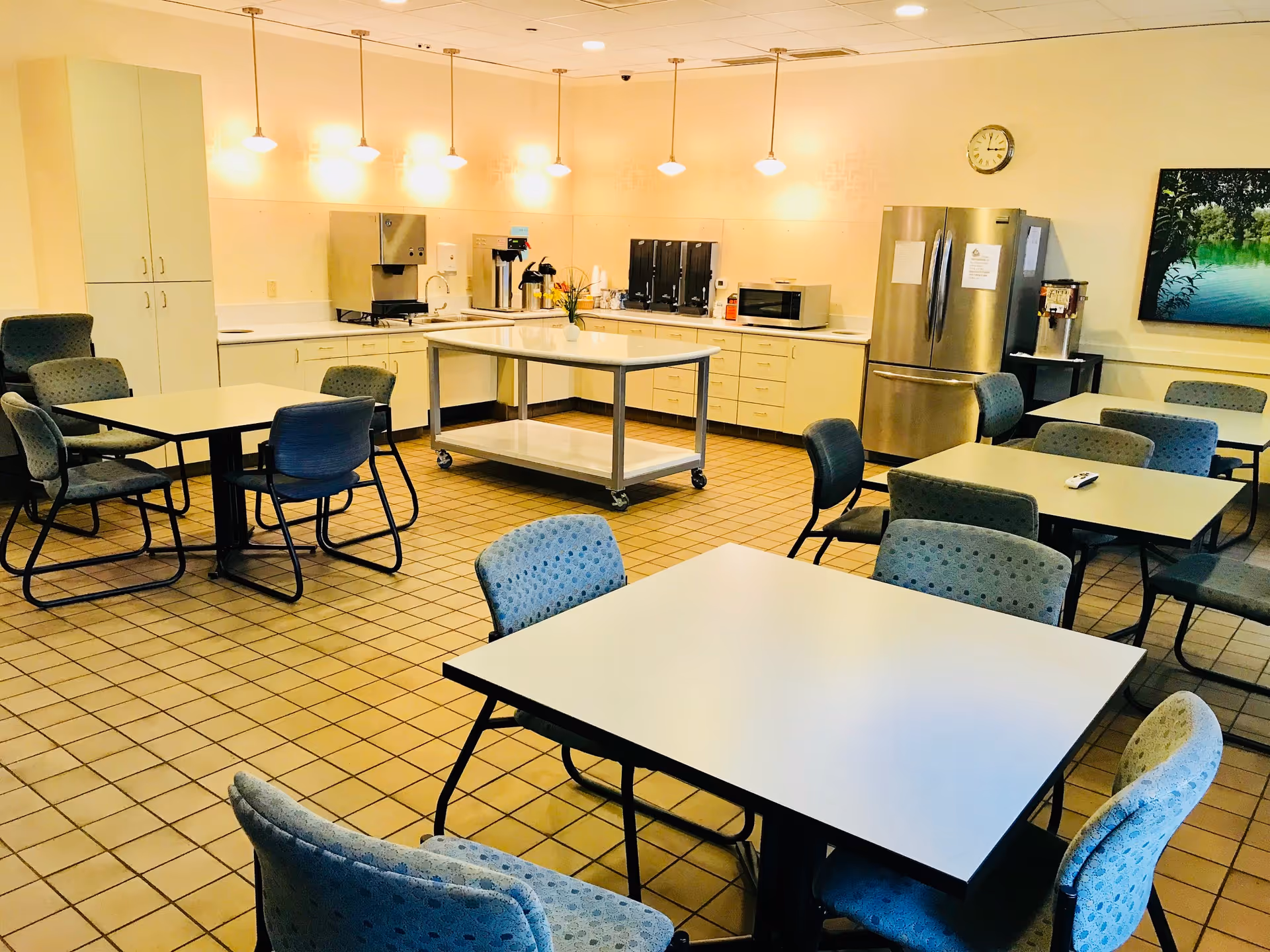 Empty communal dining room with tables and chairs, plus a kitchenette and appliances along the back.