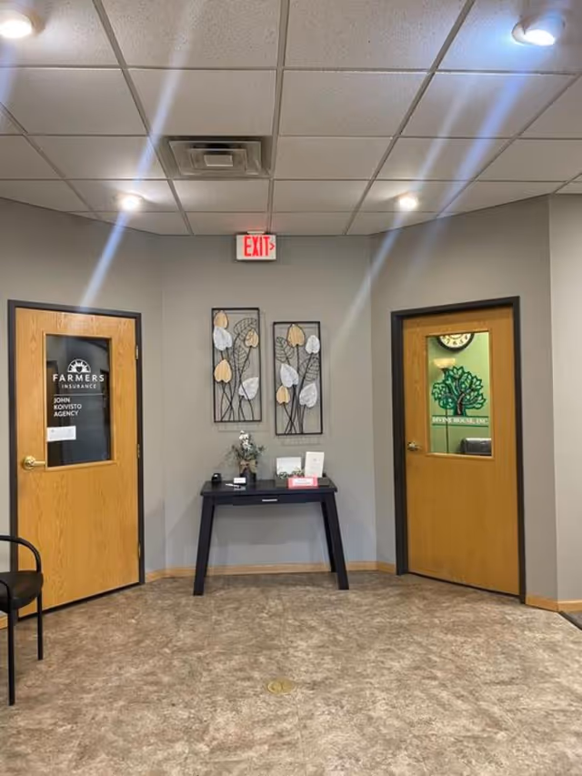 Neutral lobby area with two wooden doors, a black table, wall decor, and an exit sign.