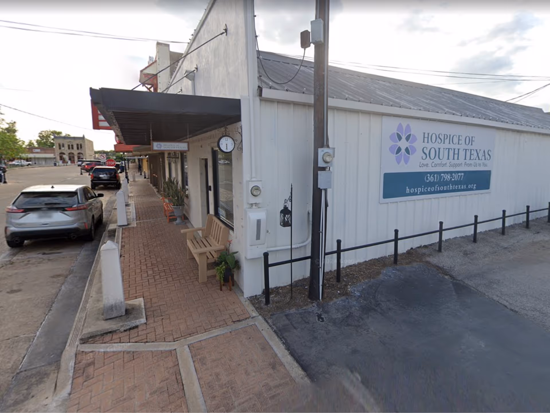 Outside view of Hospice of South Texas building with sidewalk, bench, and sign.