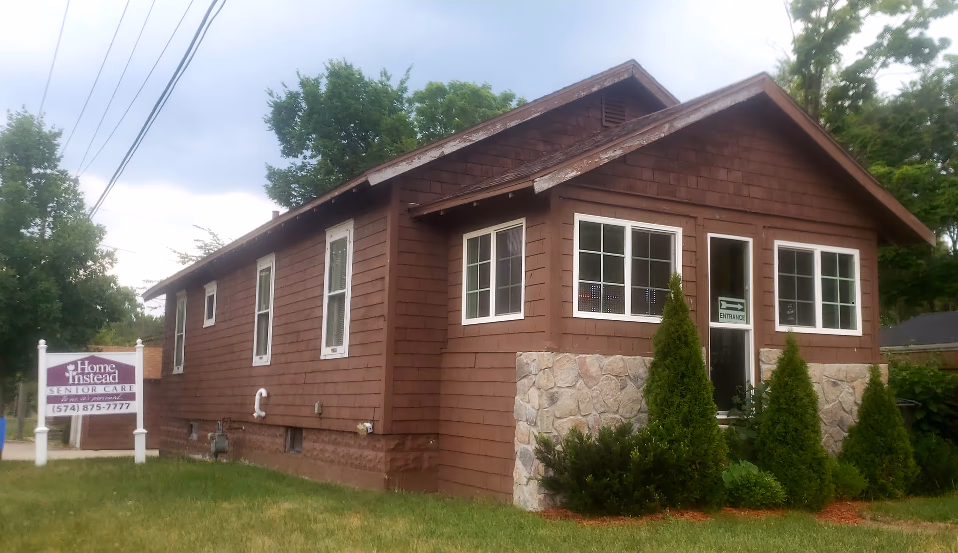 Brown one-story building with stone foundation, front entrance, and a Home Instead sign.