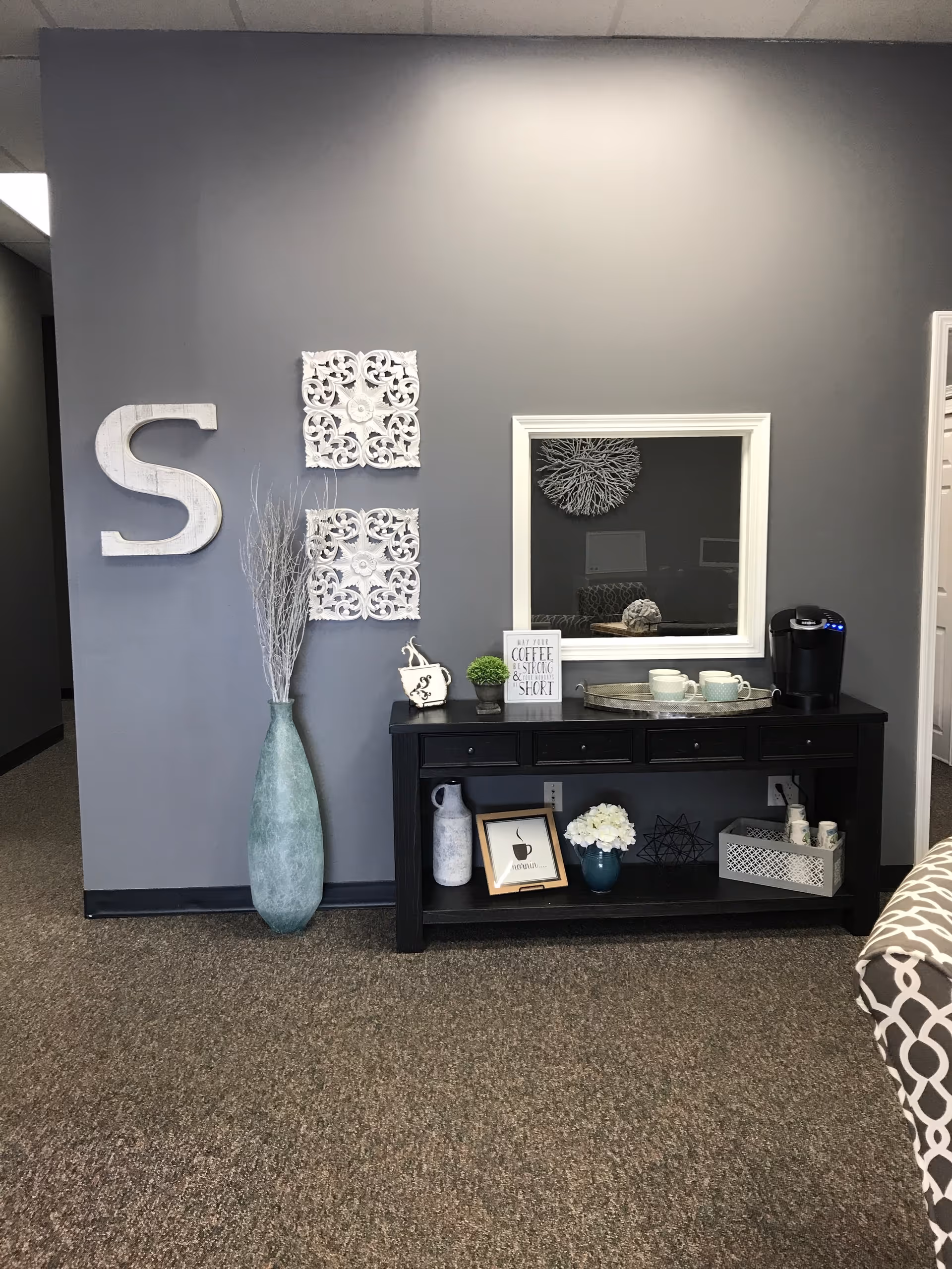 Dark console table with decor and a large white 'S' on a gray wall.