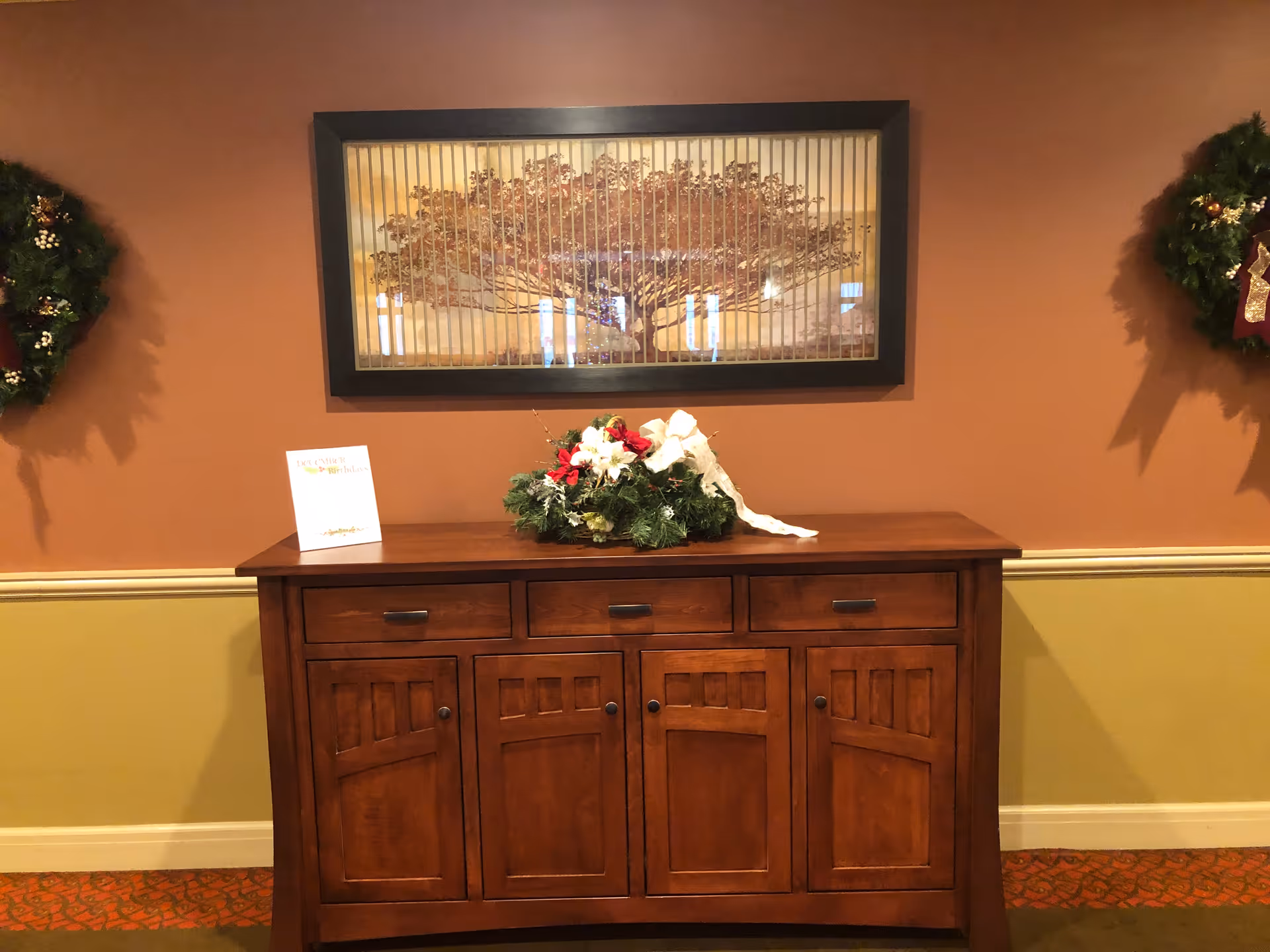 Wooden sideboard console in a VNA of Eastern Massachusetts lobby, flanked by wreaths and framed art.
