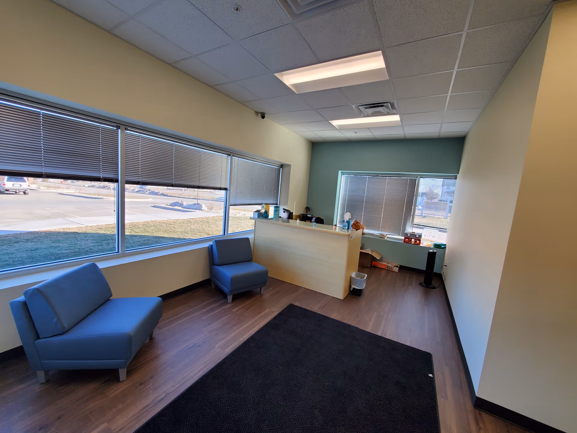 A lobby seating area with blue chairs and a reception desk beside large windows.