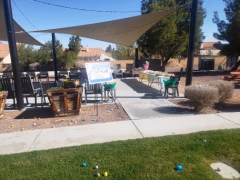 Outdoor patio area with shade sail, tables, chairs, and a display board.