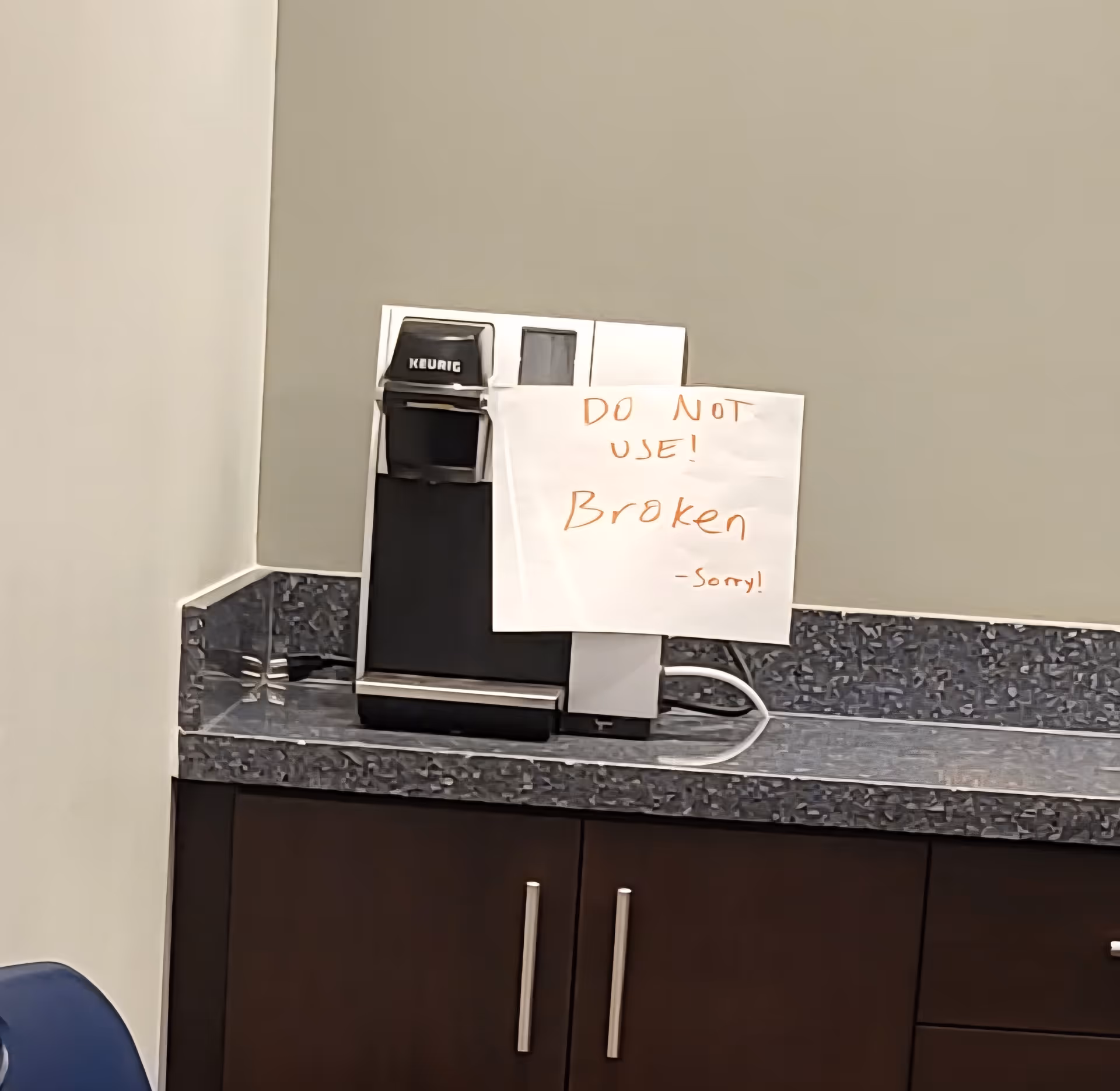Keurig coffee maker on a dark speckled counter with a handwritten Do Not Use! Broken note.