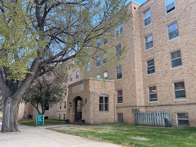 Exterior view of a brick multi-story building with arched entrance and trees.