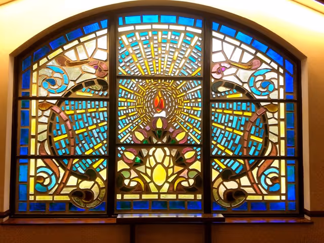 Colorful stained-glass window with geometric patterns and floral centerpiece indoors.