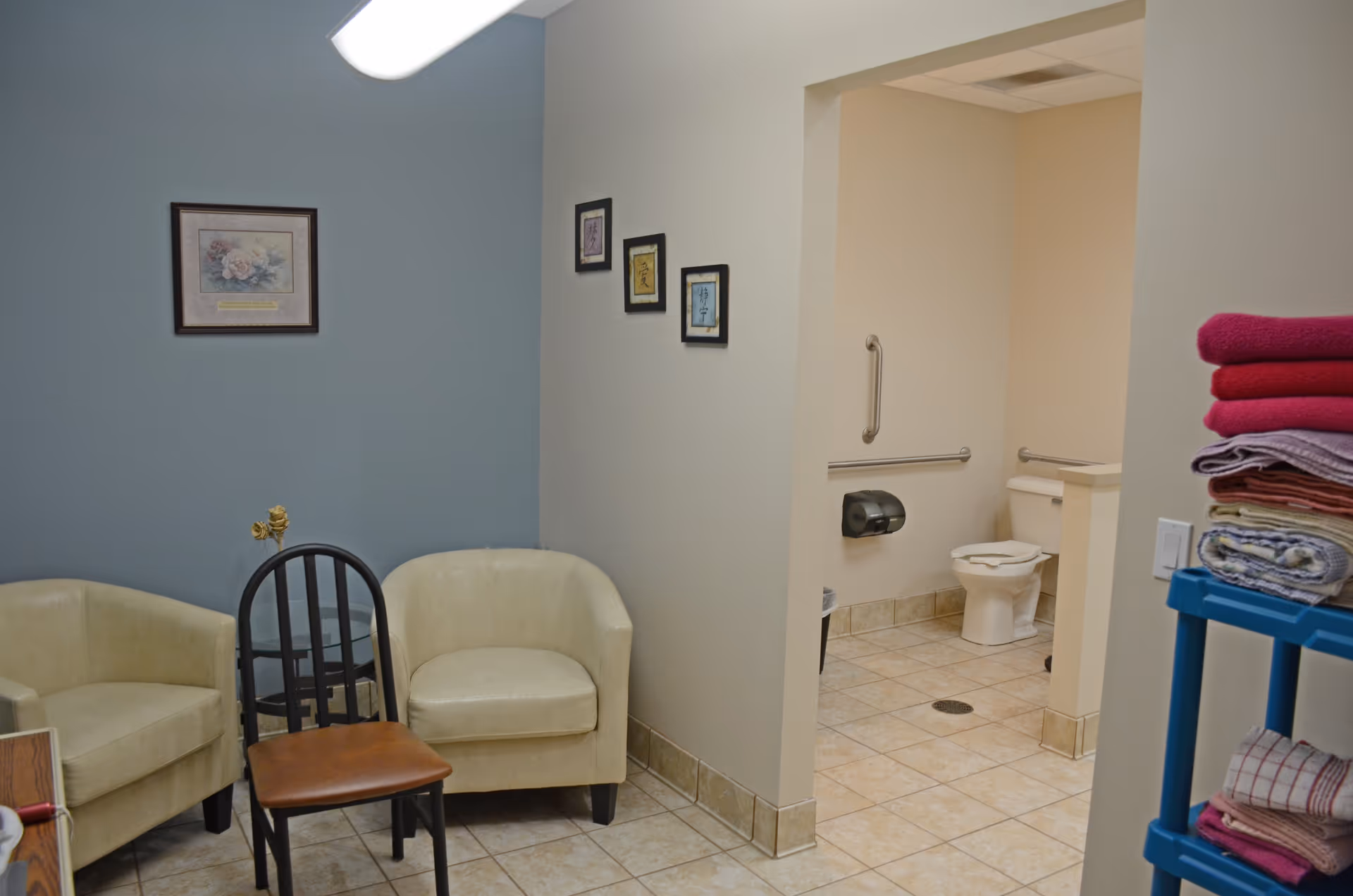 Small seating area in a senior center with beige chairs, a black chair, and tiled floor.