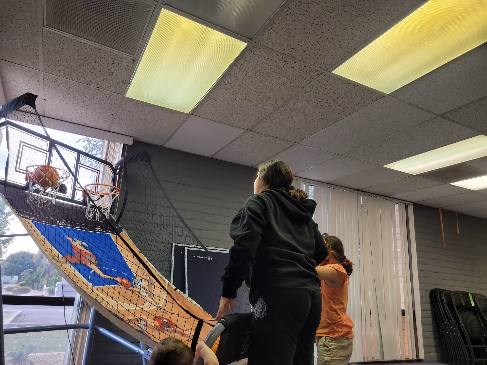 Indoor activity room with a basketball arcade game and two people nearby.