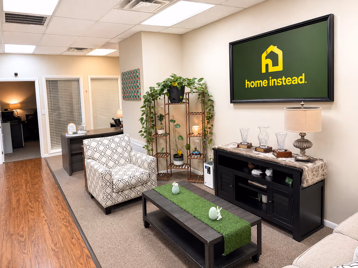 Interior senior living lounge with a Home Instead sign, seating, plants, and a coffee table.