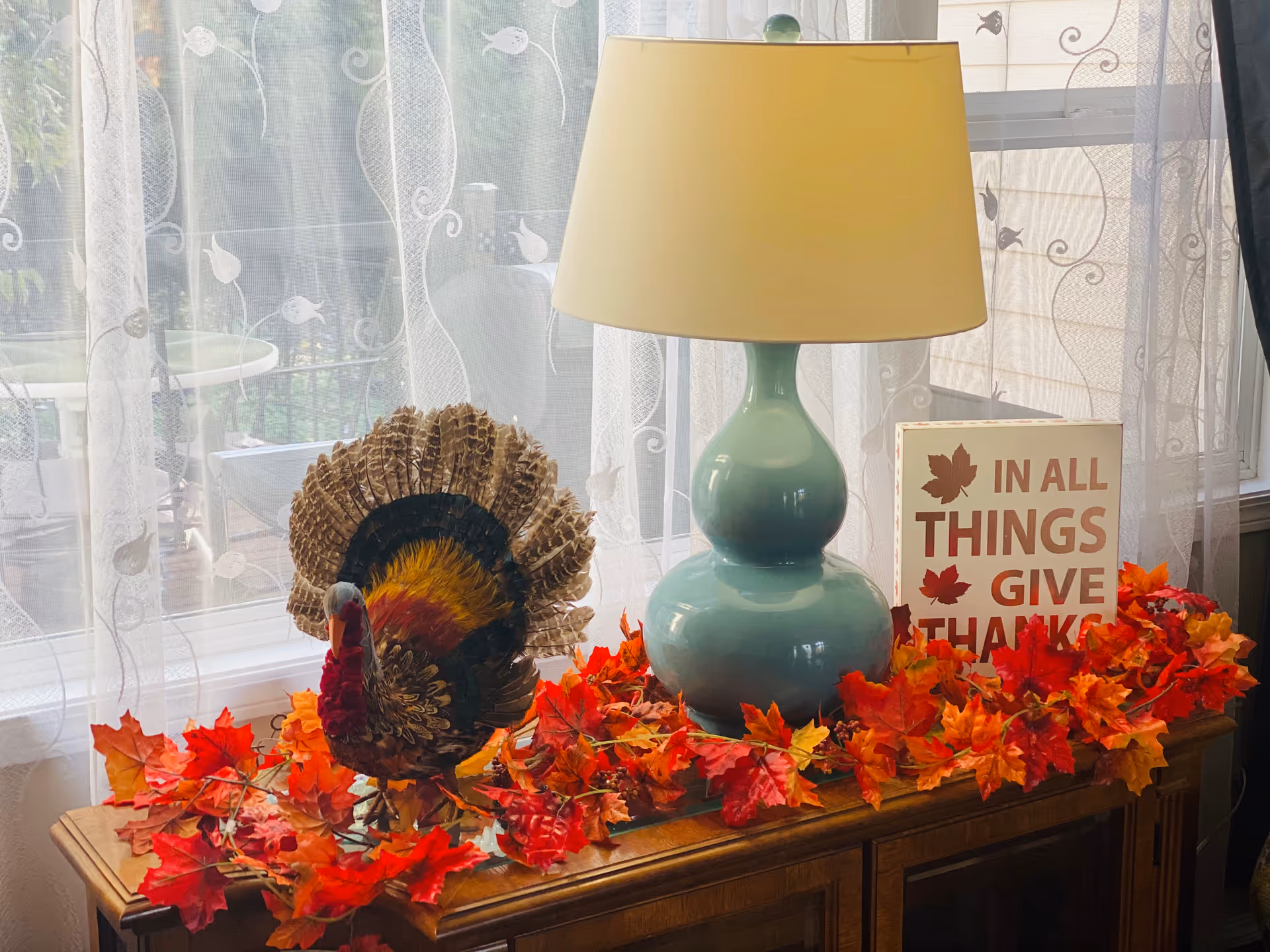 Autumn-themed decor on a wooden table with a lamp, leaves, and a thankful sign.