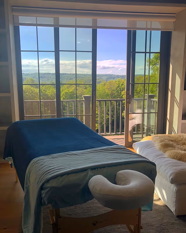 Massage table with blue cover in a bright room with balcony doors.