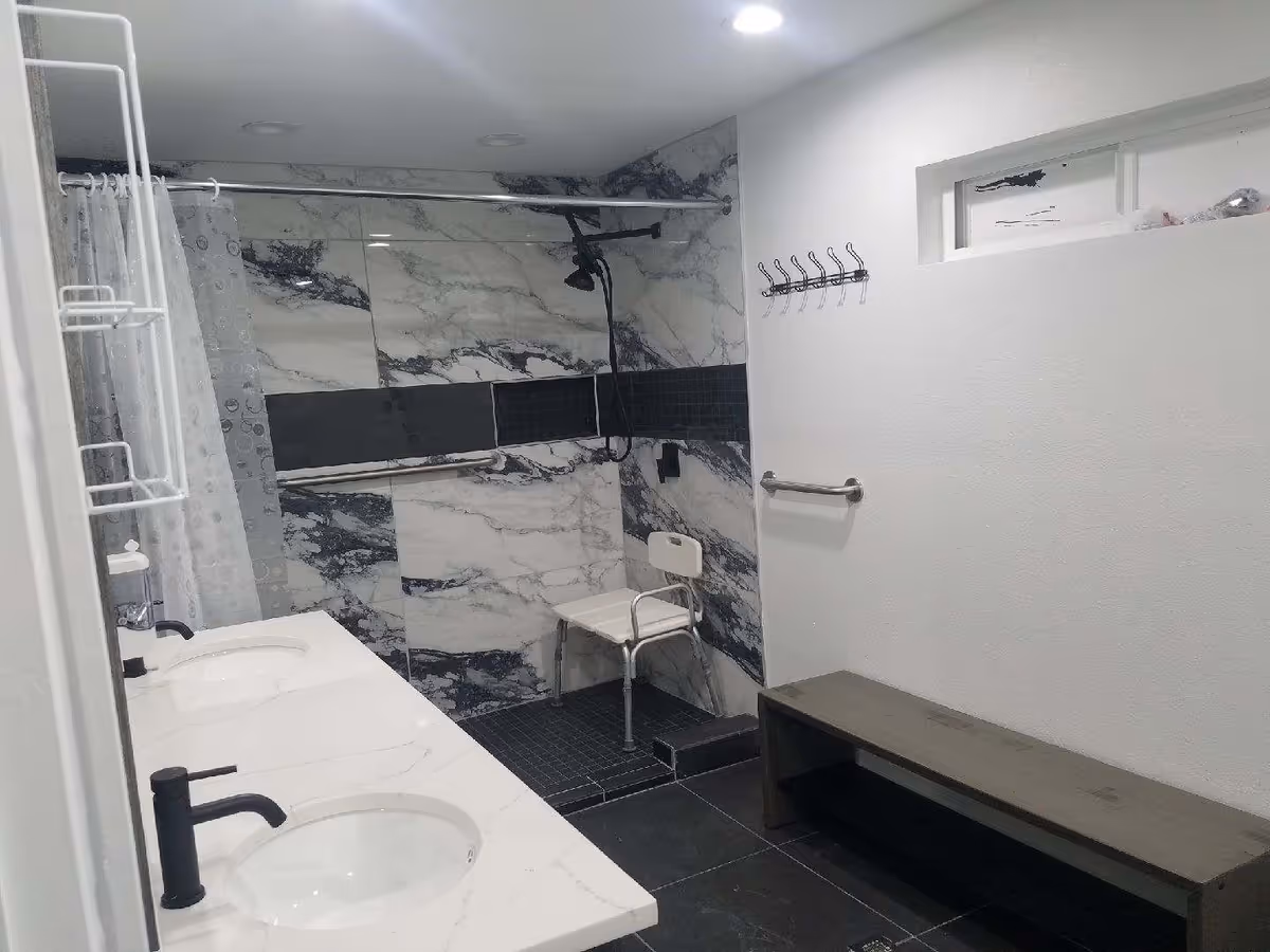 Modern bathroom with marble-tiled shower, dual sinks, and a bench.