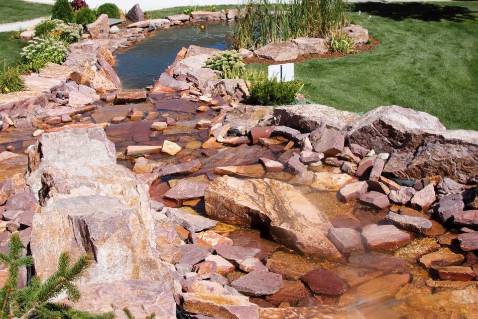 Outdoor rock water feature with a flowing stream and manicured lawn.