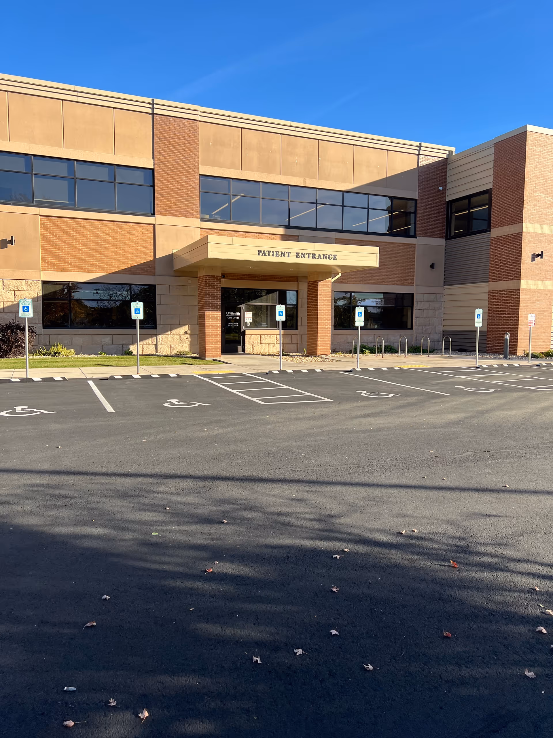 Brick medical facility exterior with patient entrance, large glass windows, and accessible parking in front.