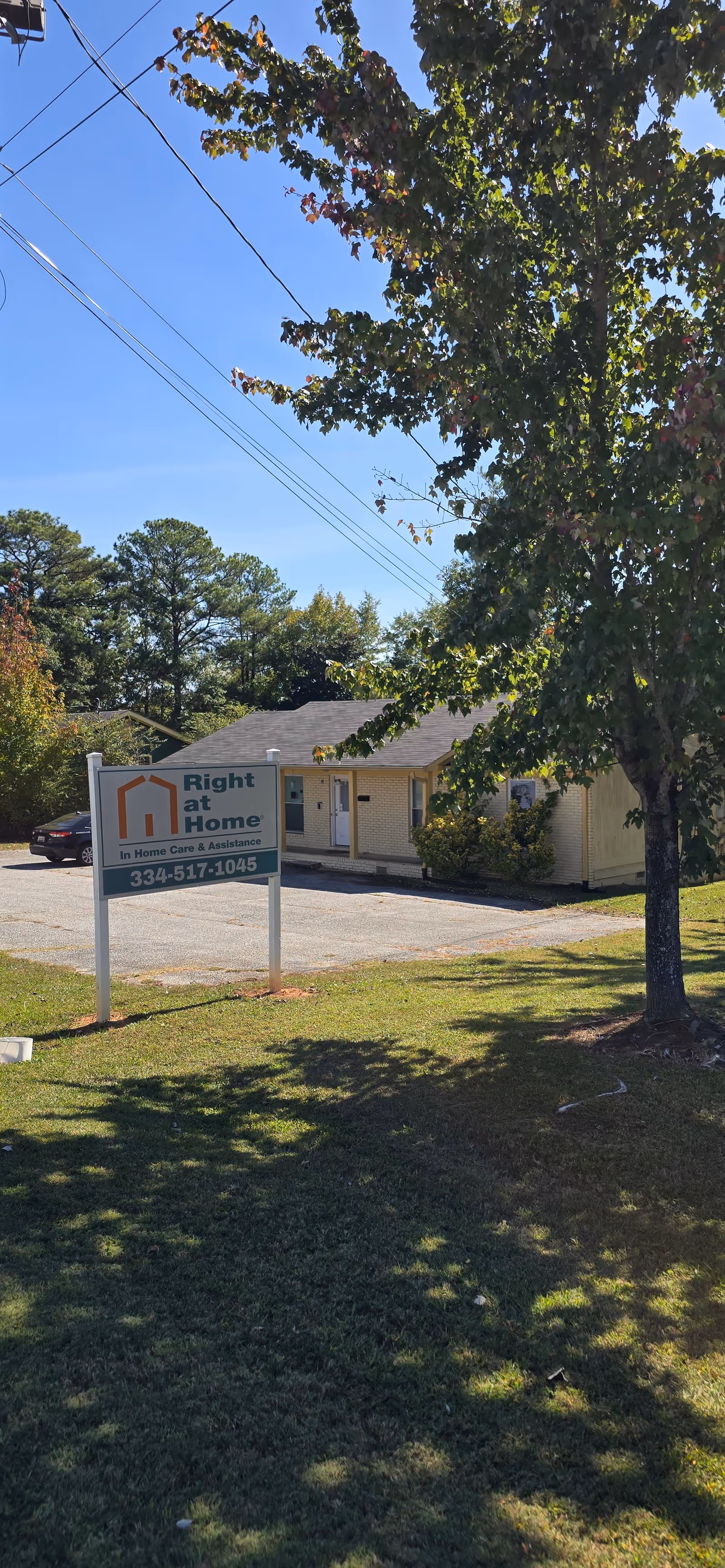 Exterior view of Right at Home facility with sign, parking lot, trees, and blue sky.