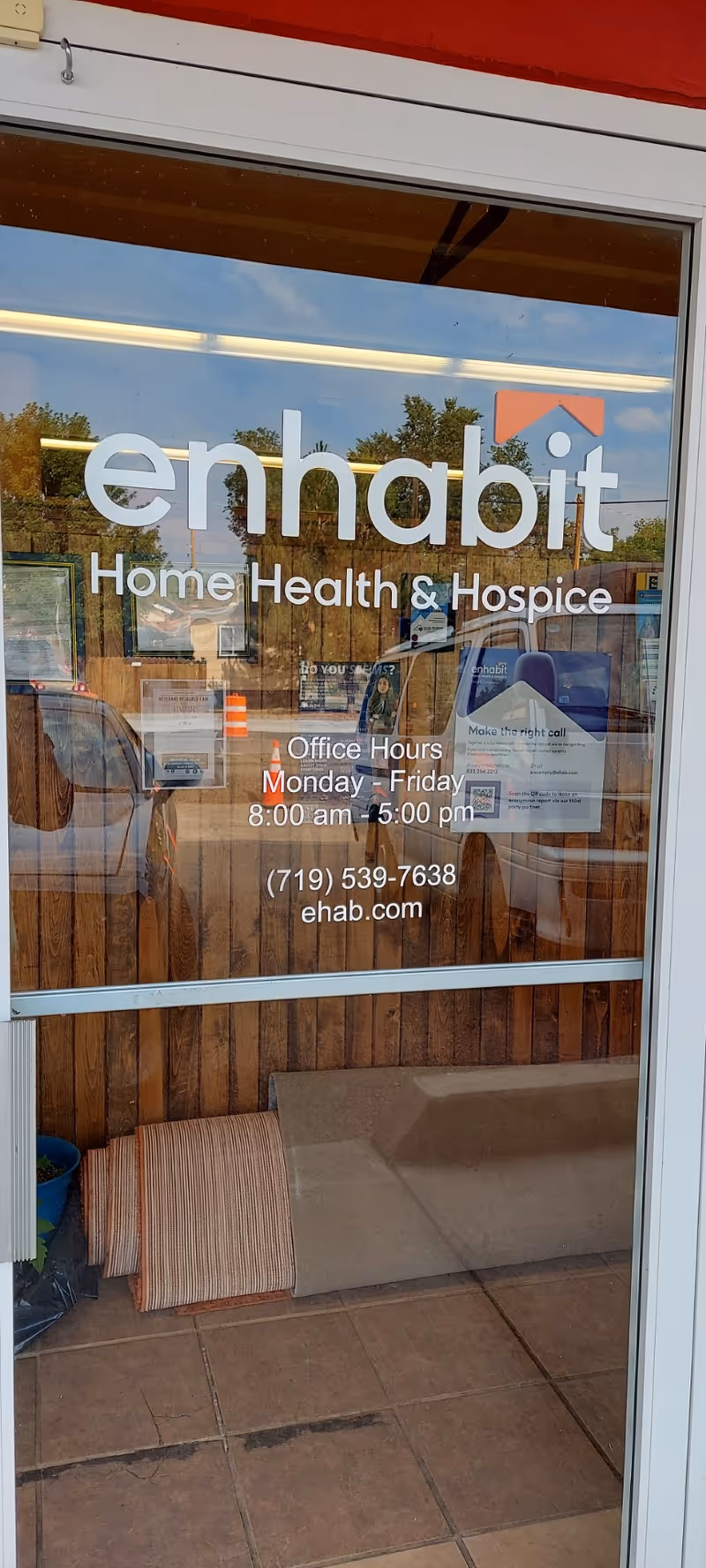 Glass storefront door displaying Enhabit Home Health & Hospice sign with office hours.