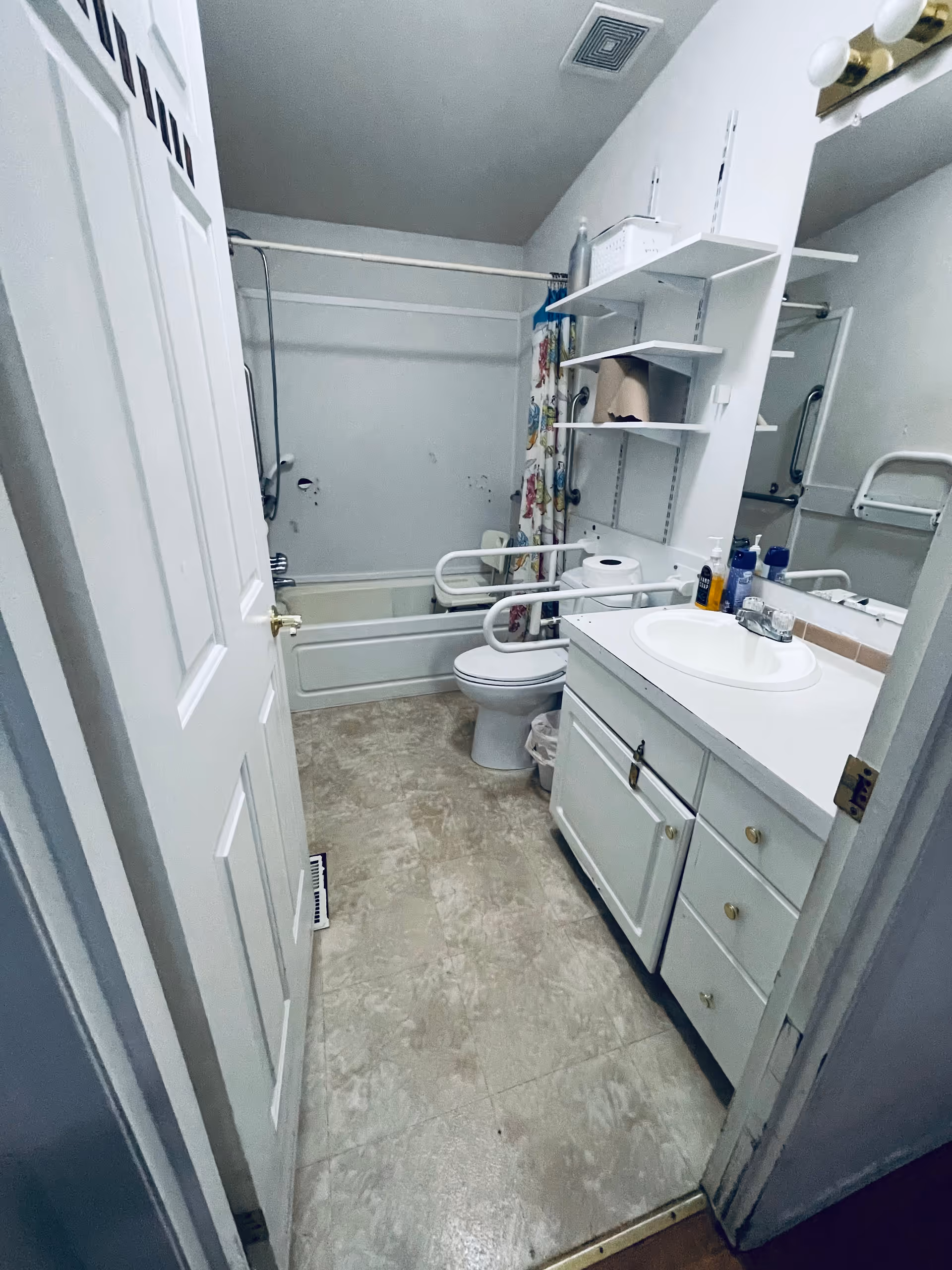 Compact bathroom in a senior home with bathtub, toilet, sink, and shelves.