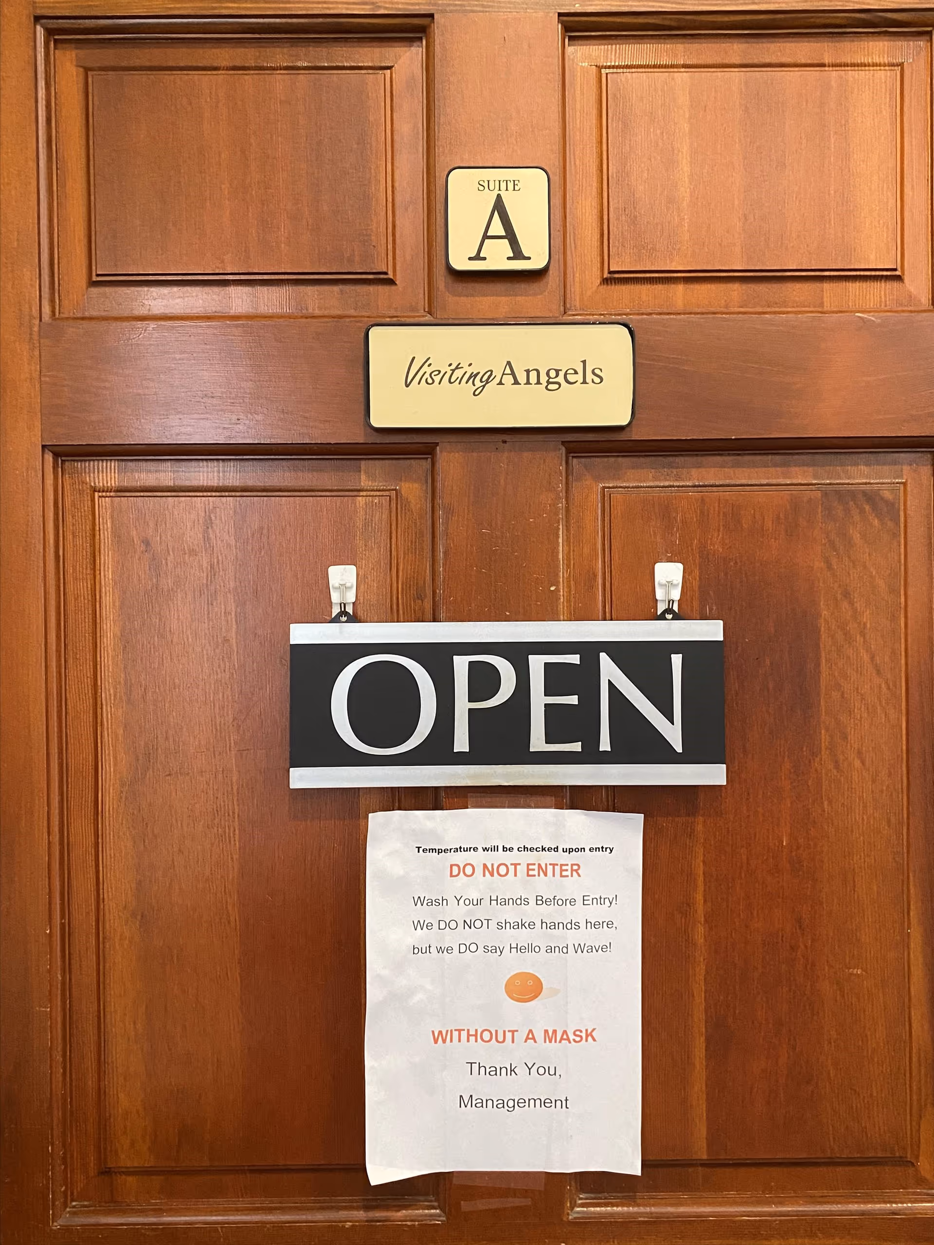 Wooden facility door with Visiting Angels suite sign and an OPEN notice.