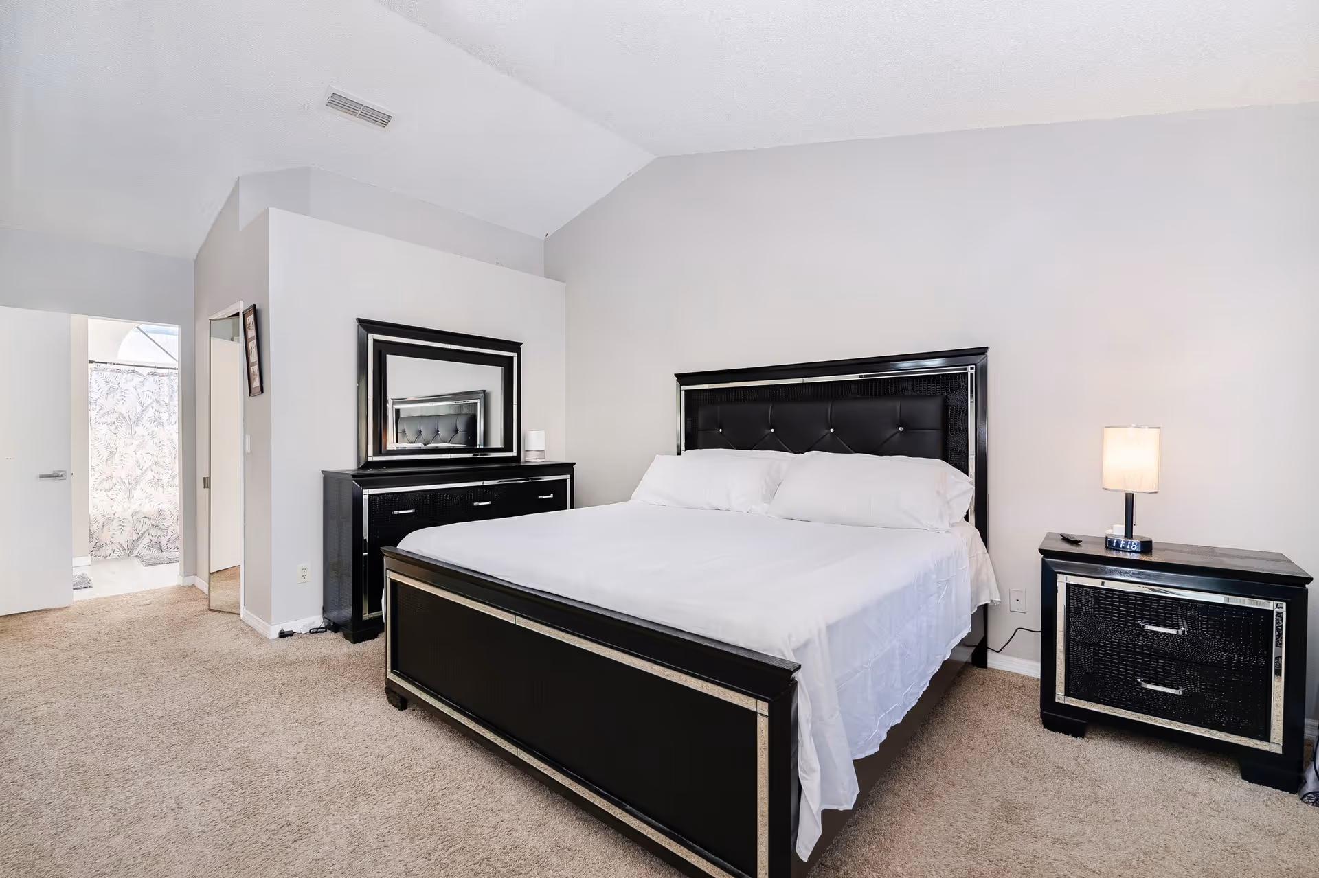 A spacious bedroom with a dark bed, matching dresser and nightstands, and neutral walls.