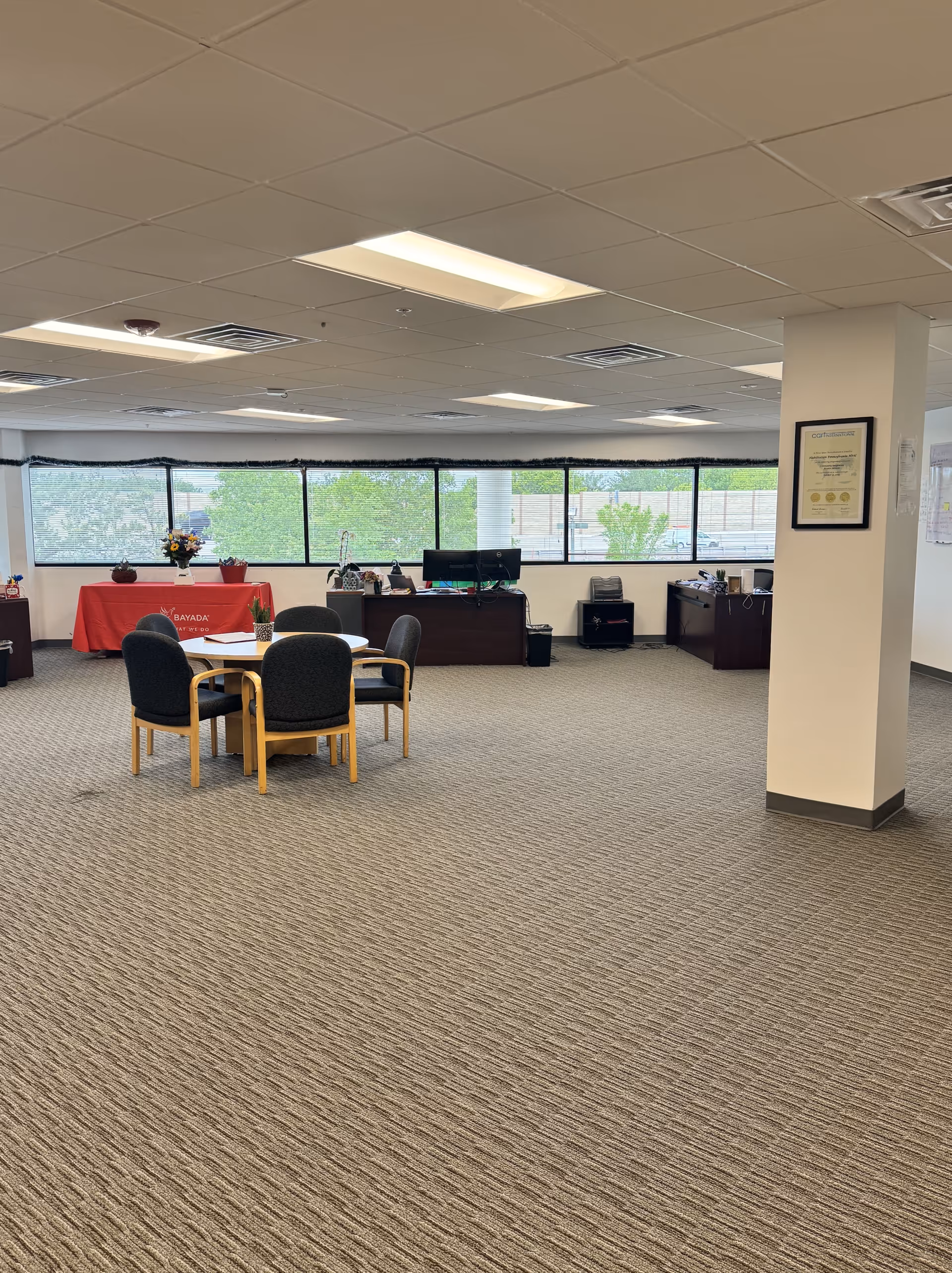 Open interior lounge area with round table, chairs, and reception desk by large windows.
