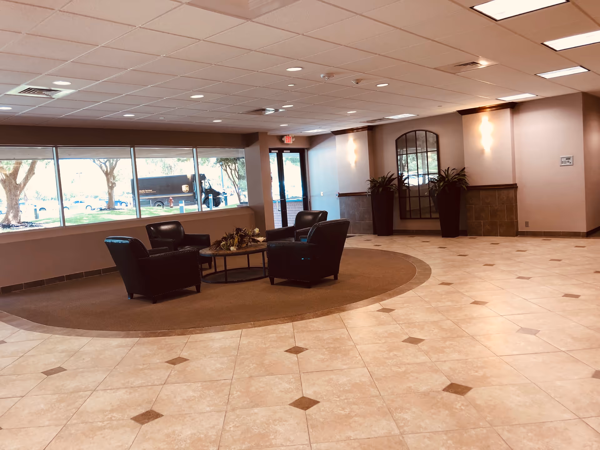 Indoor lobby with leather chairs around a circular rug near large windows.