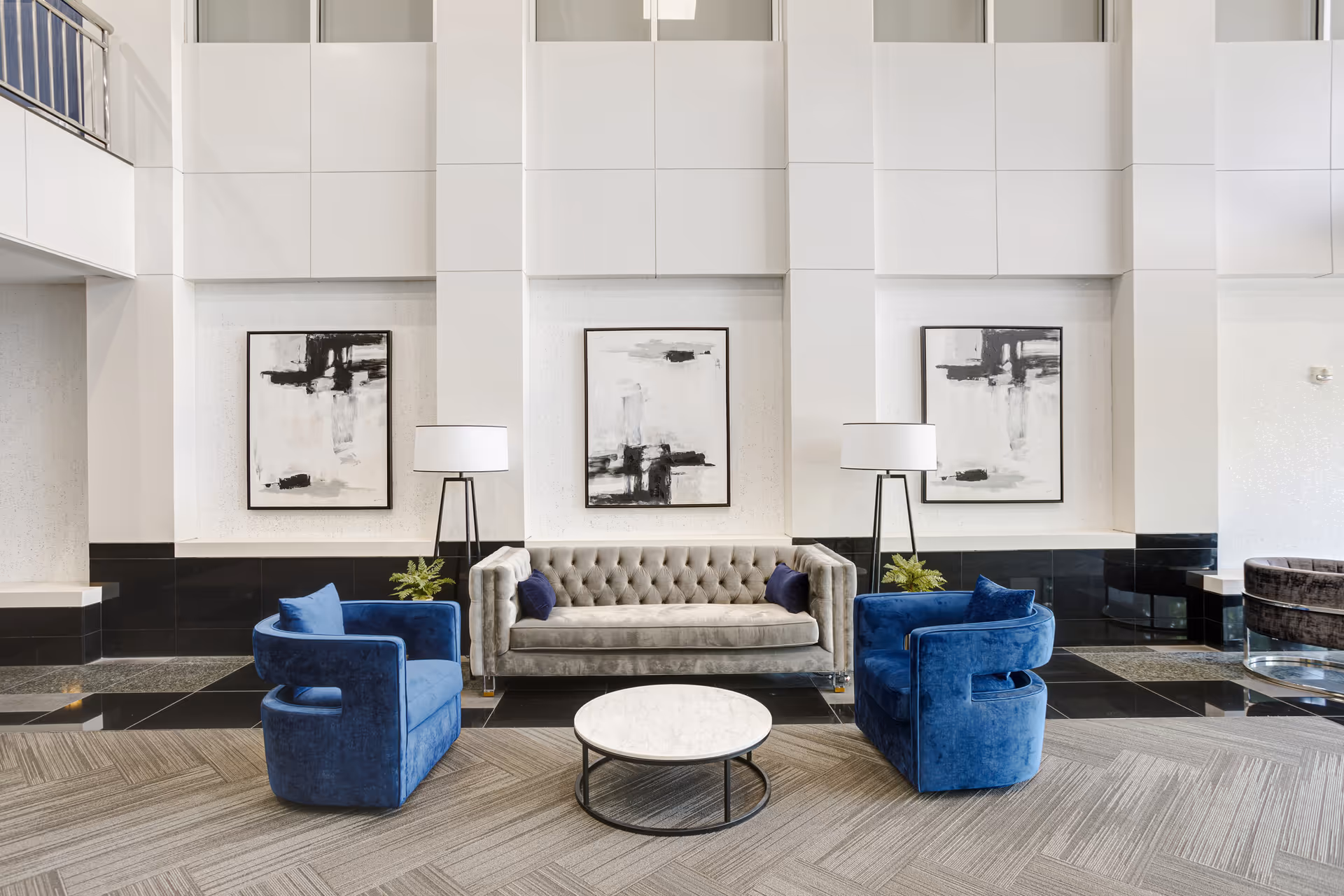 Modern hotel-style lobby with gray tufted sofa, blue chairs, marble coffee table, and abstract art.