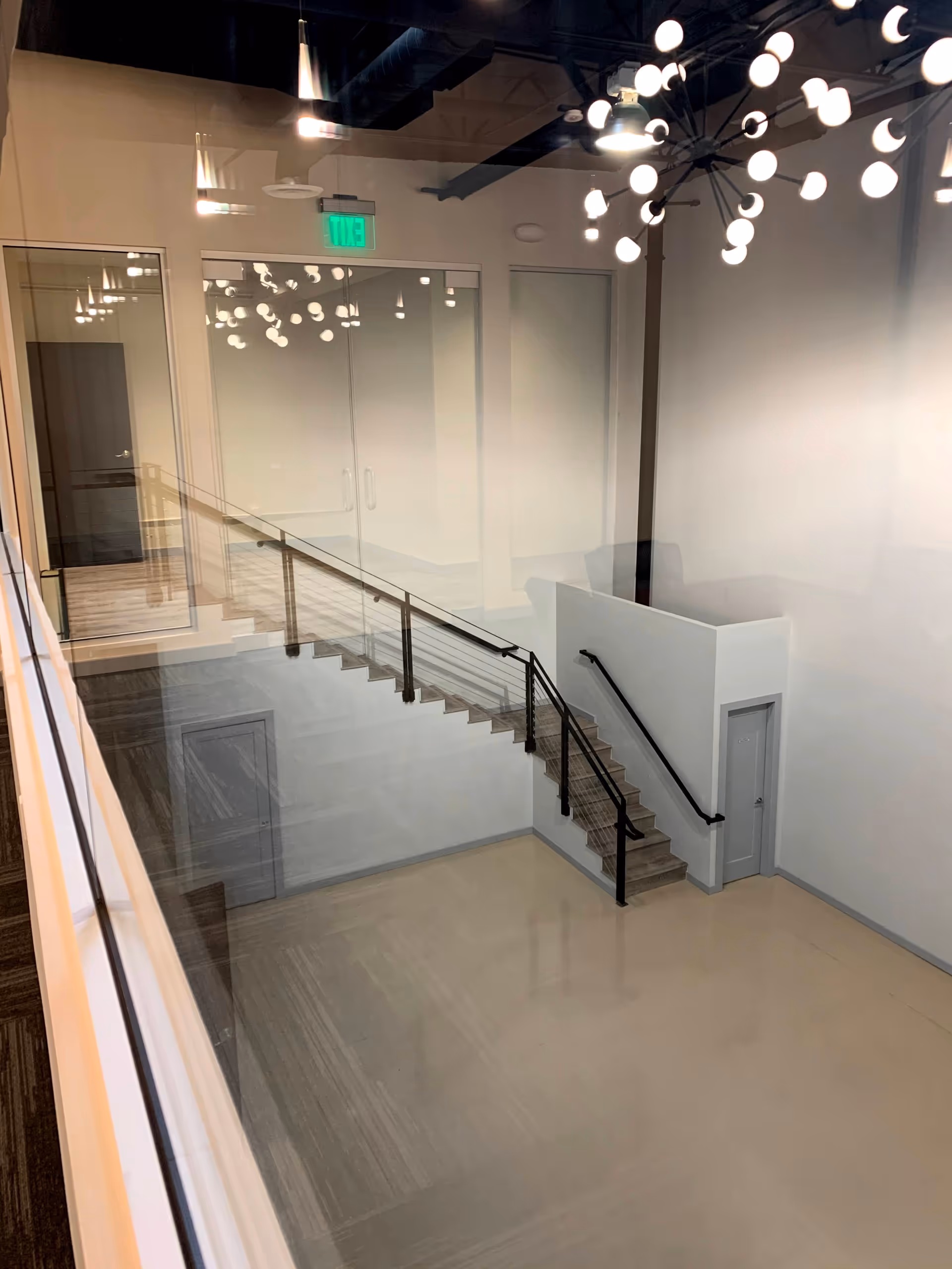 Interior view of a modern stairwell with glass railings and hanging light fixtures.