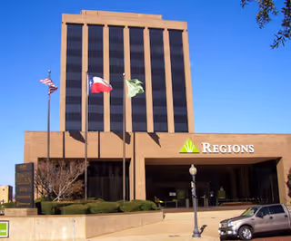 Brick Regions Bank building with three flags and a parked car in front.
