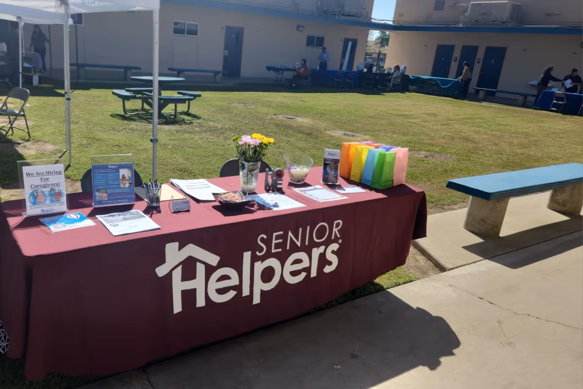 Outdoor courtyard booth for Senior Helpers with a maroon table and flyers.