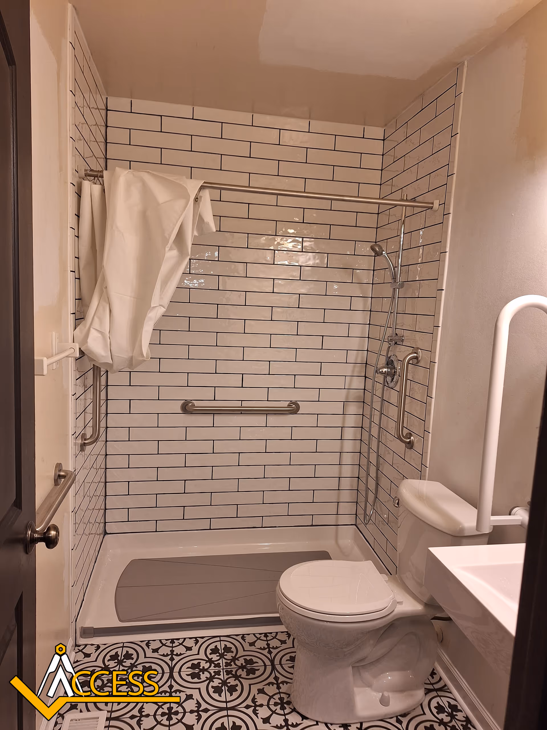 Accessible bathroom with tiled shower, grab bars, toilet, and patterned floor tiles.