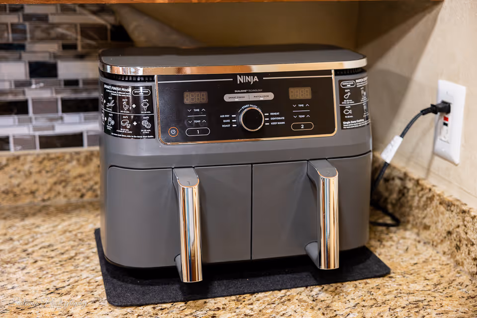 Grey Ninja air fryer sits on granite kitchen counter with tiled backsplash.