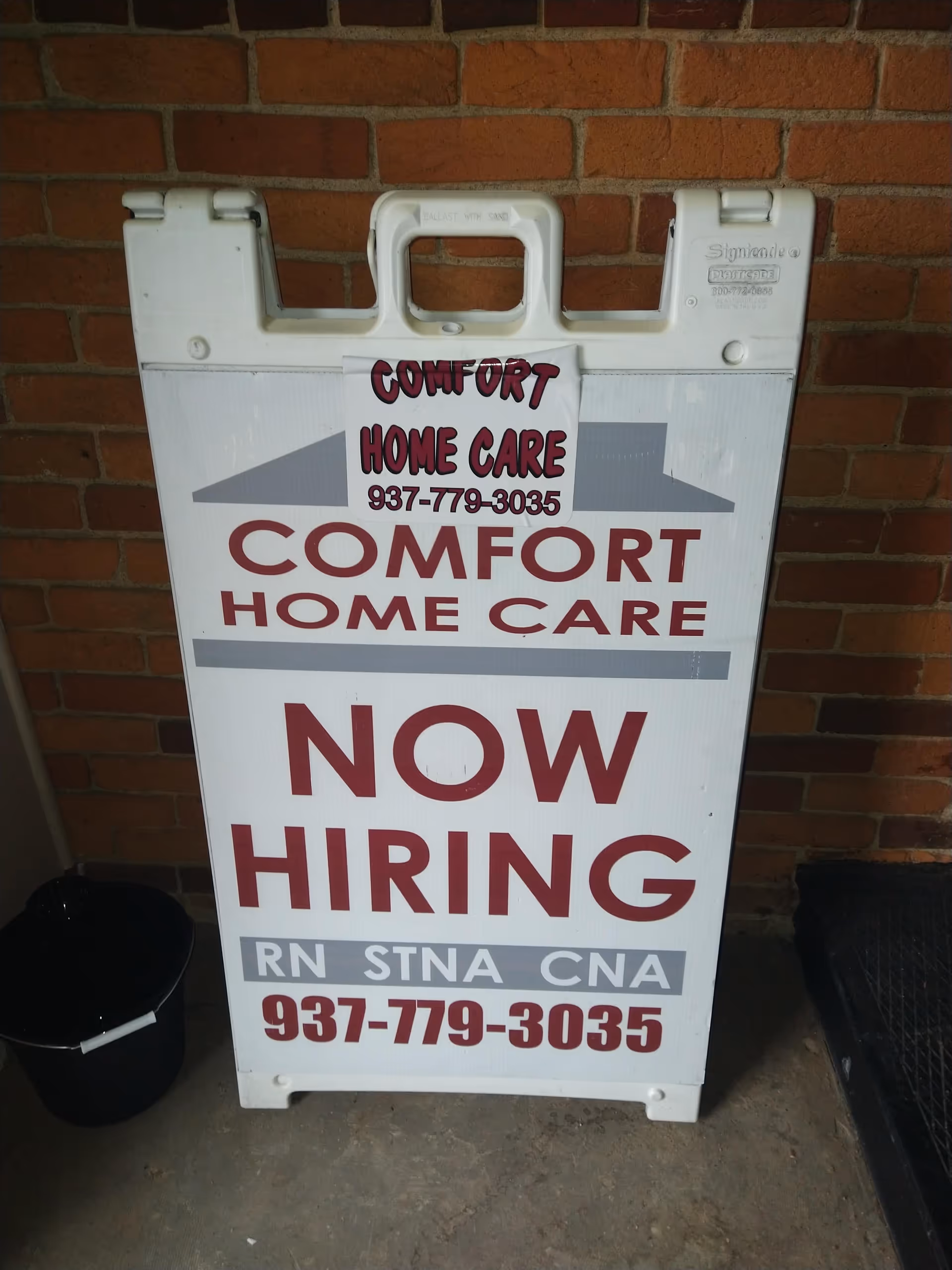 White signboard on brick wall advertising Comfort Home Care and now hiring.