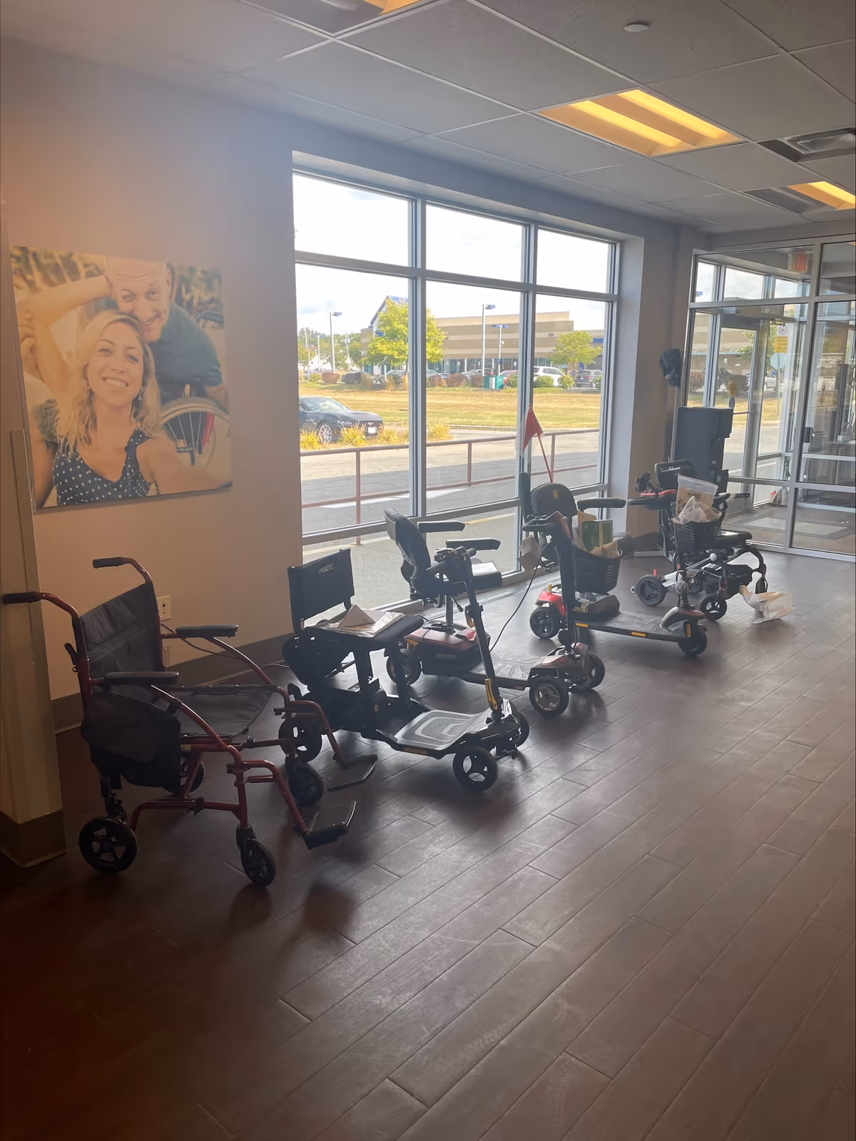 Interior lobby with several mobility aids (wheelchairs, walkers) lined up near large windows.