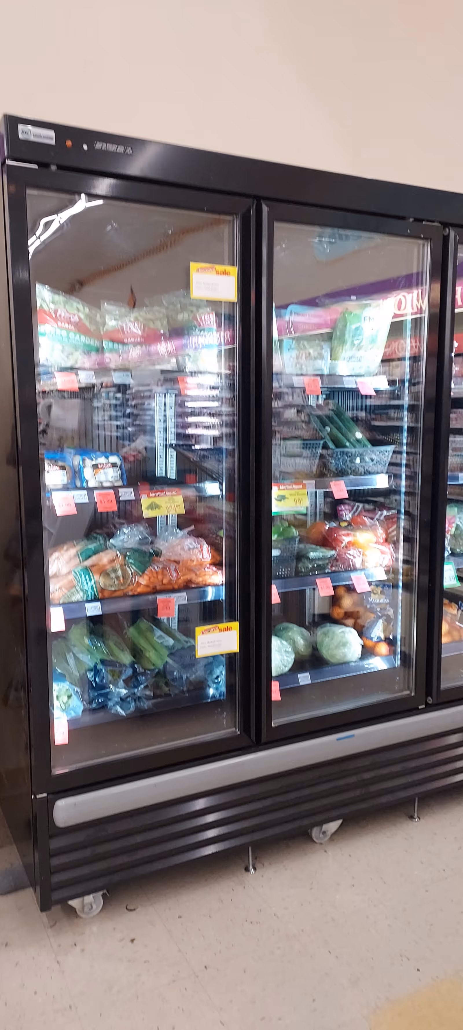 Interior view of a Discount Drug Mart glass-door refrigerated display with vegetables and groceries.