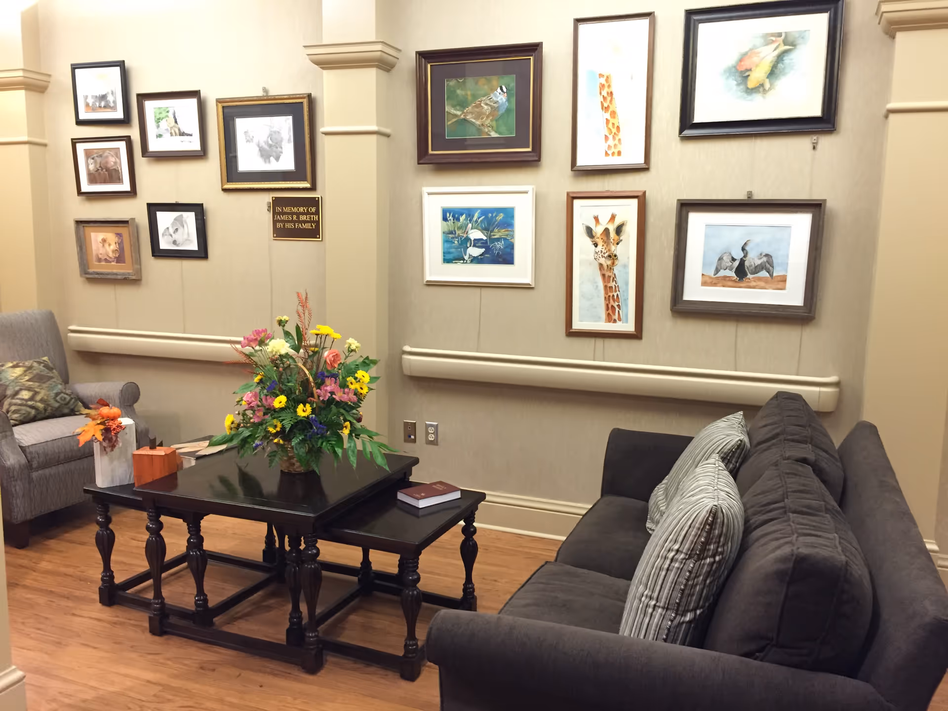A cozy living room in a senior facility with sofas, coffee table, and wall art.