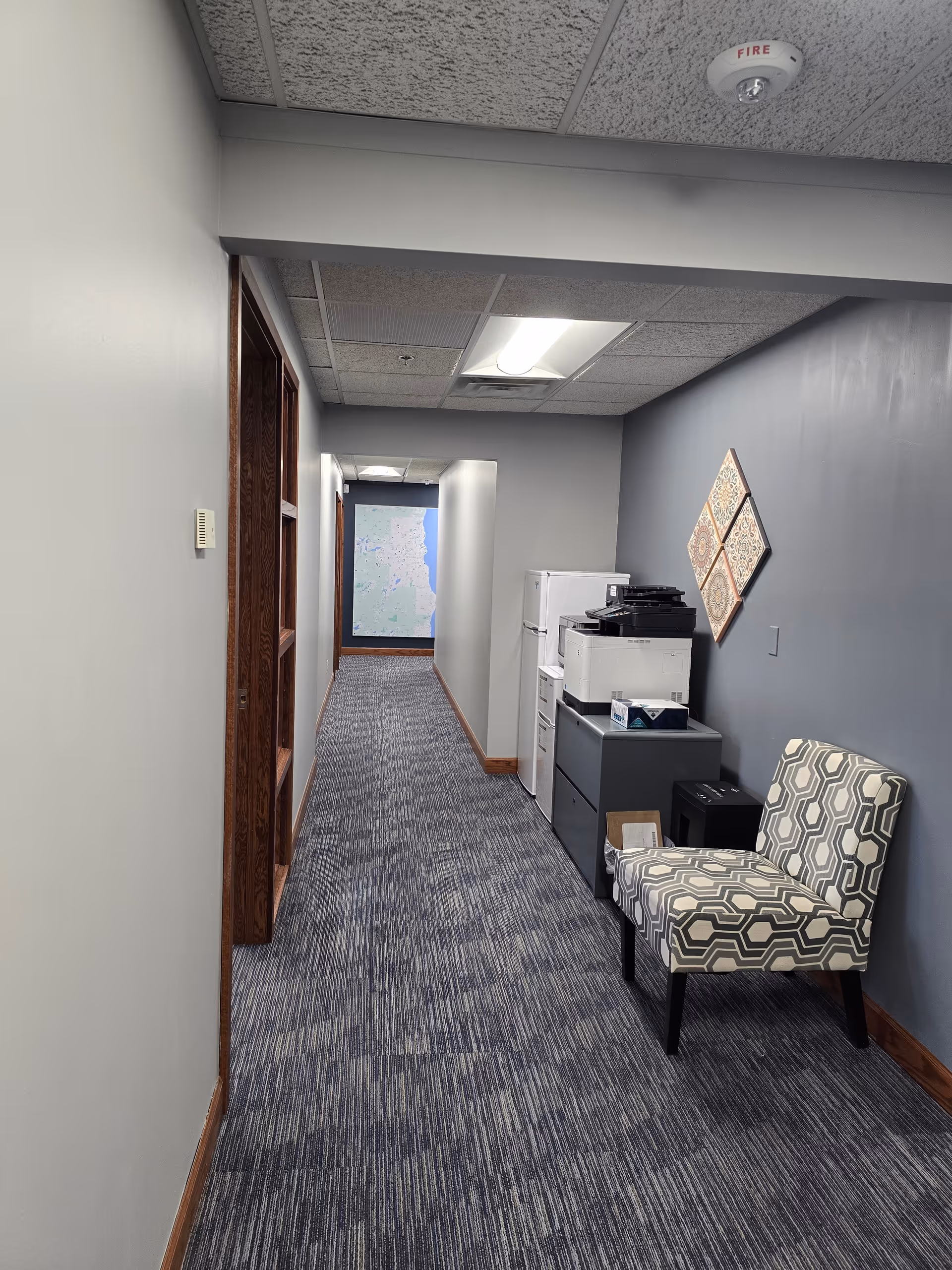 Interior corridor at Amada Senior Care with a patterned chair, printers, and a wall map.