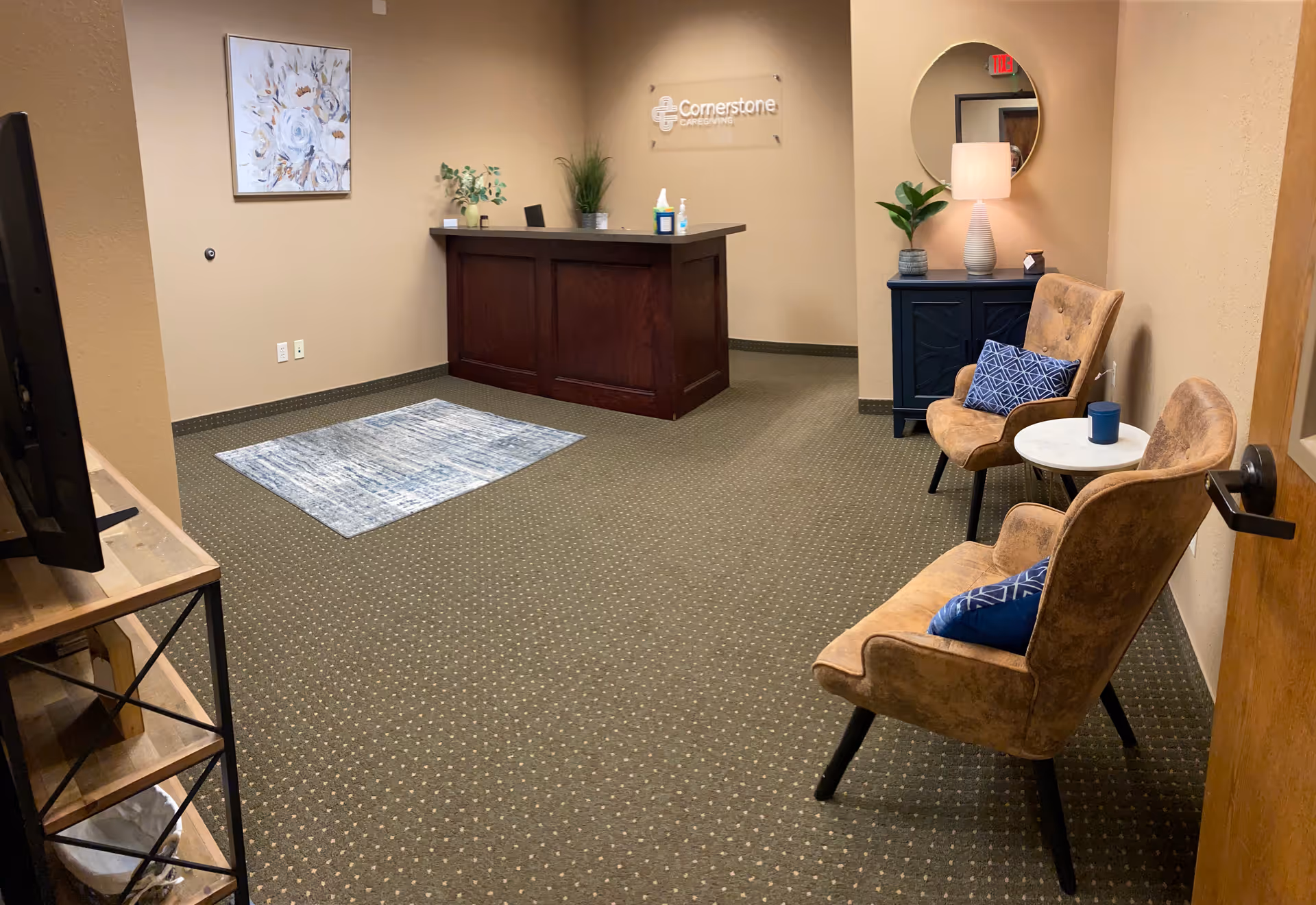 Reception desk in a beige interior lobby with seating, plants, lamp, and round mirror