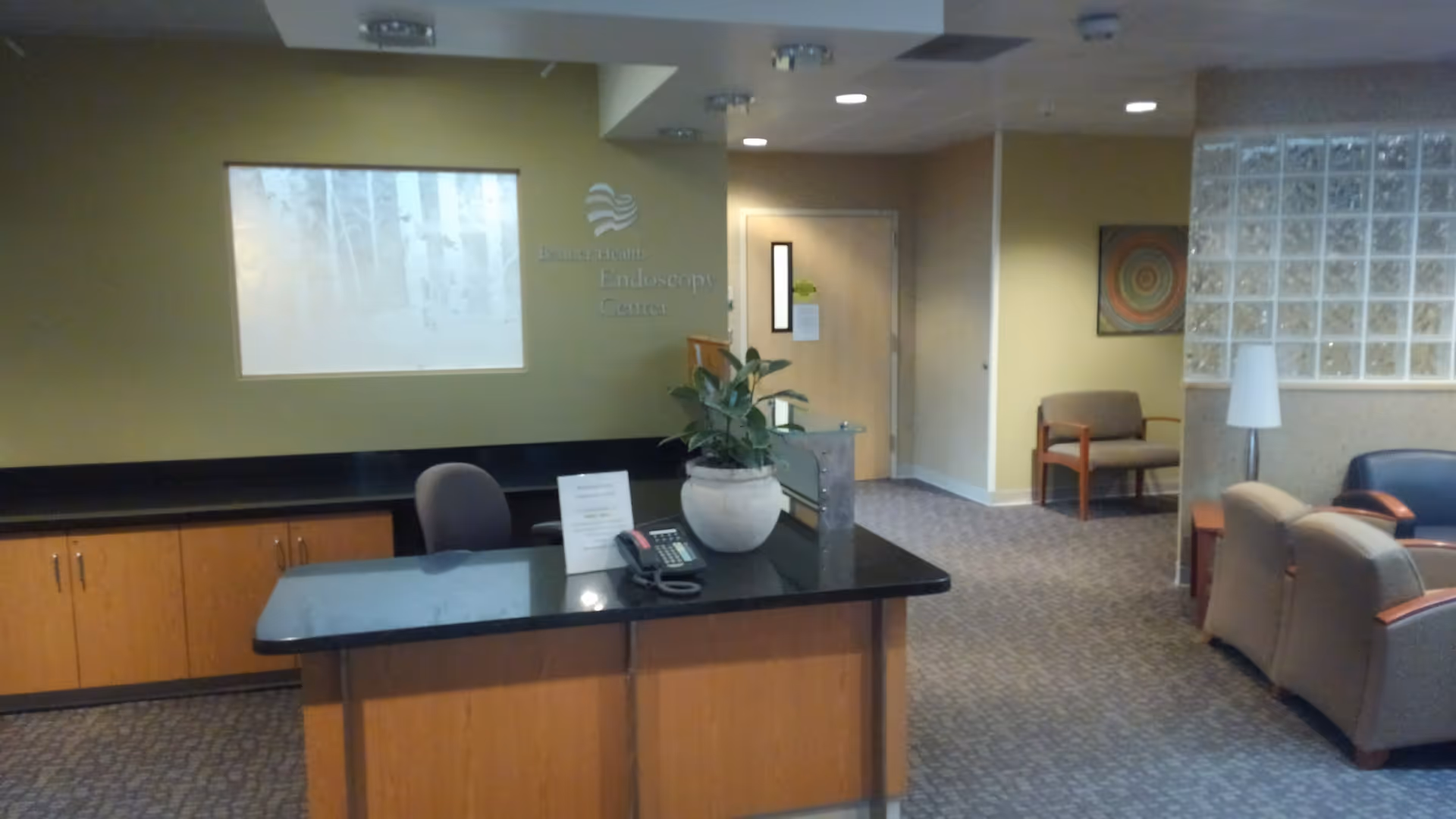 Hospital reception desk in a spacious interior lobby with seating, plant, and glass block wall.