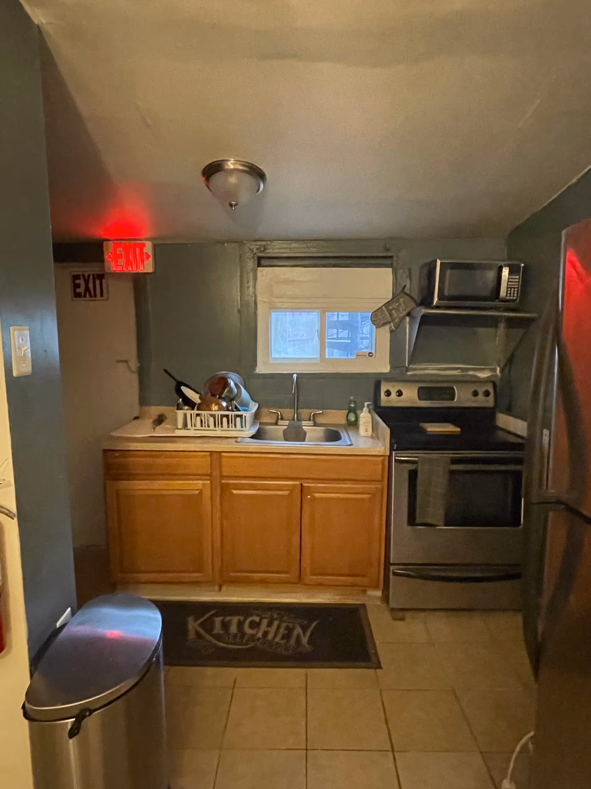 Small kitchen with sink, stove, microwave, dish rack, and wooden cabinets.