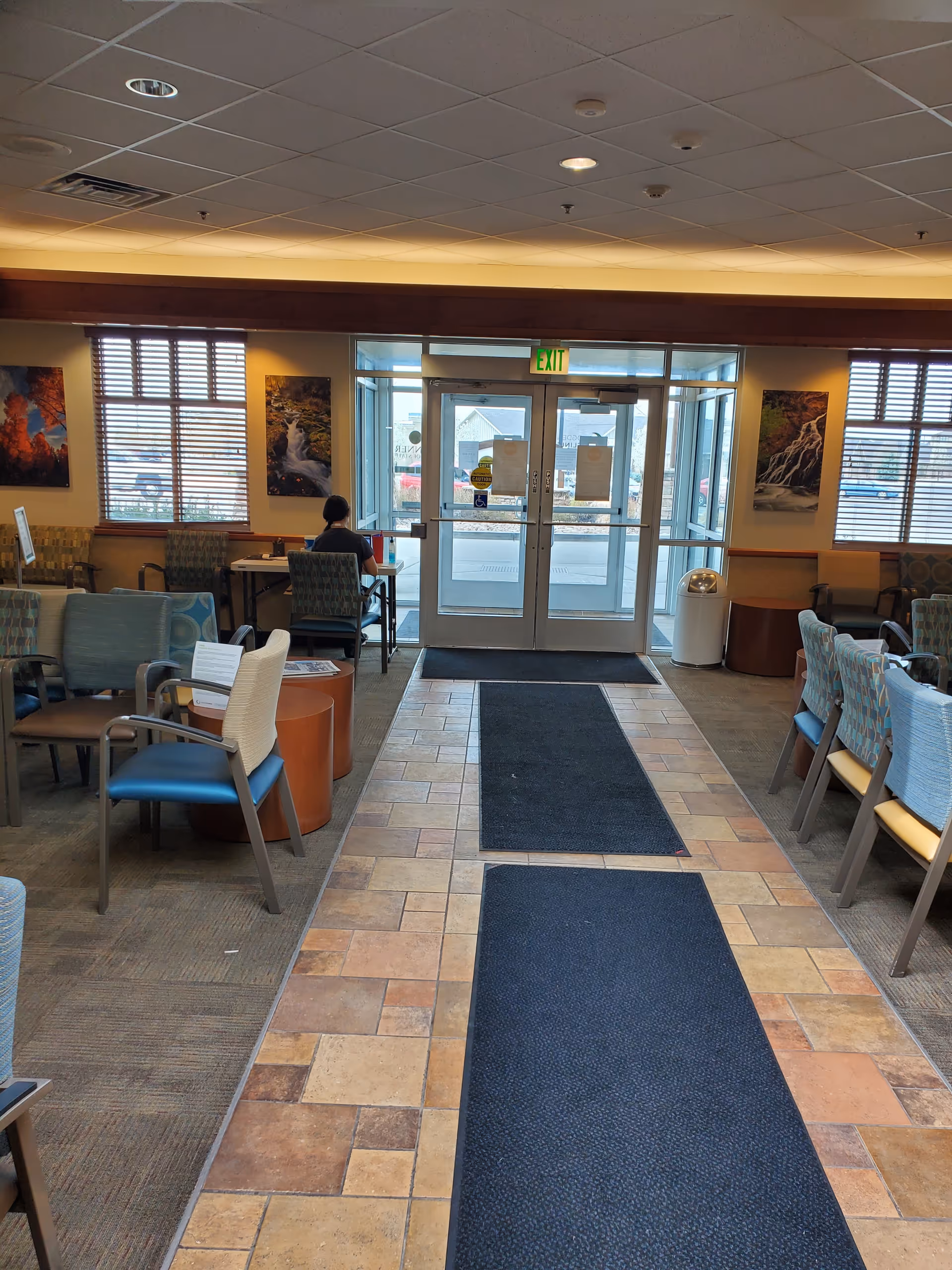 Lobby area with seating along walls, glass doors, exit sign, and a person seated.