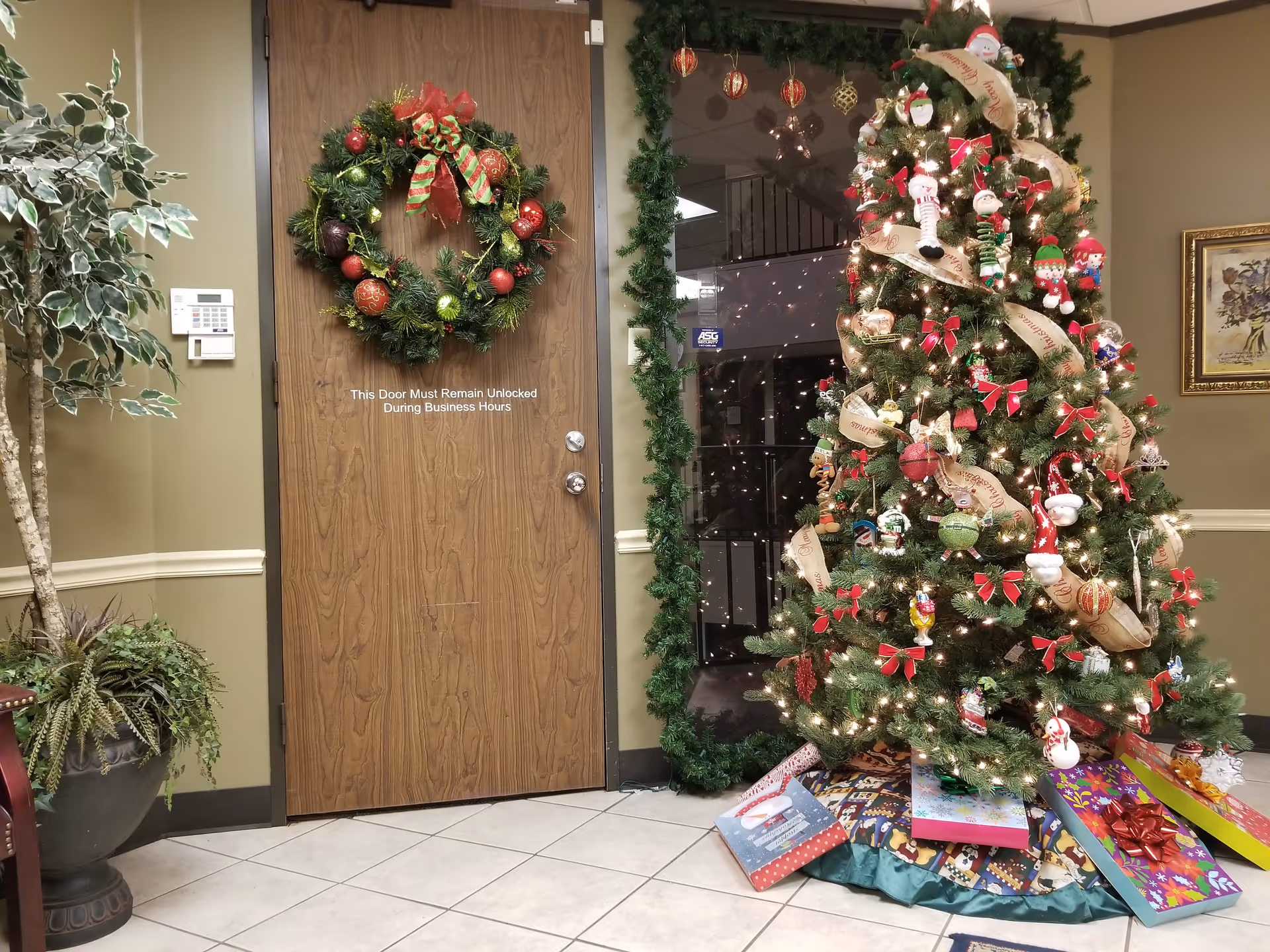 A festive Christmas tree and wreath decorate an indoor lobby beside a wooden door.