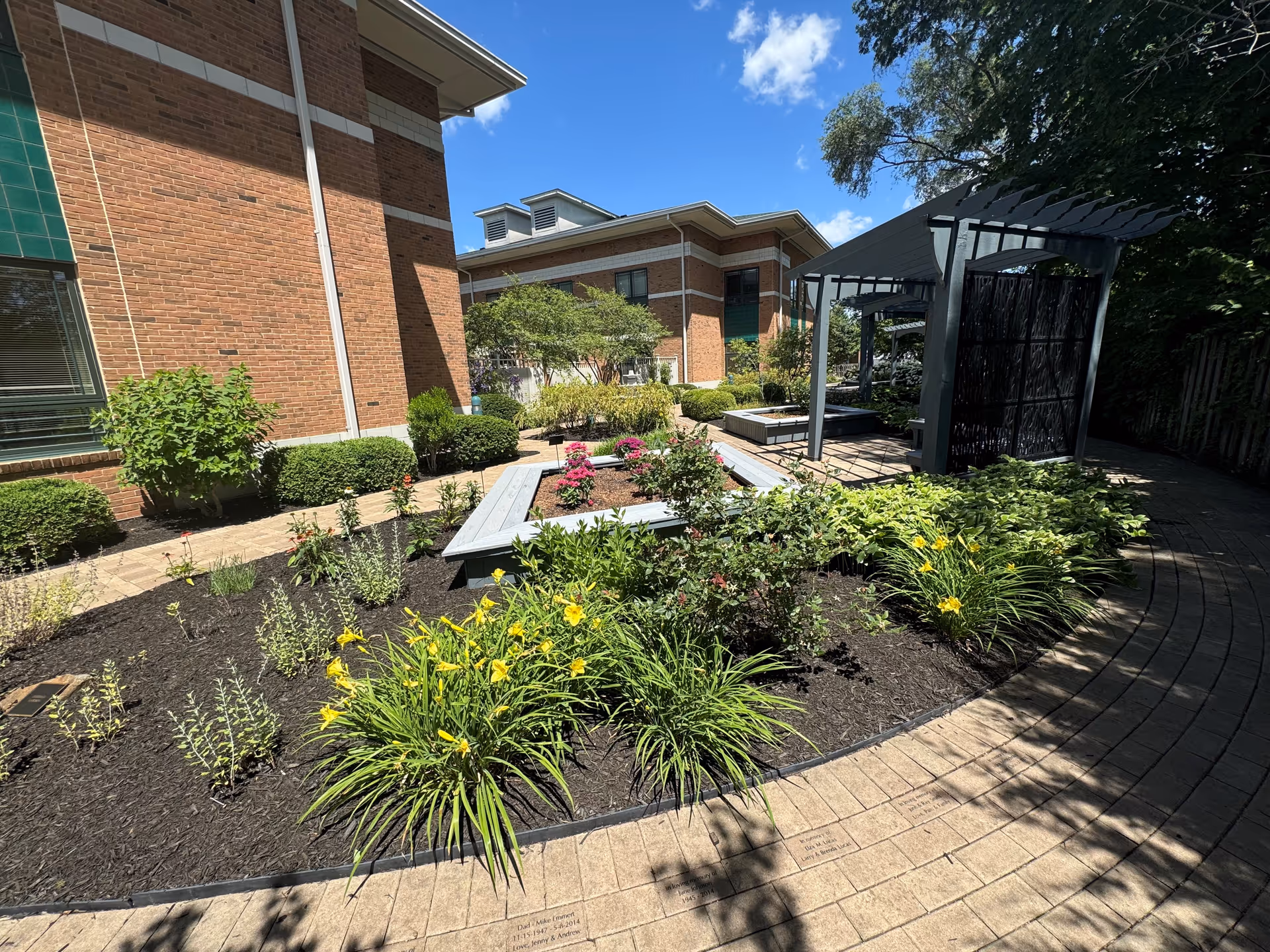 Brick facility walls surround a landscaped outdoor courtyard with shrubs, flowers, and a pergola.
