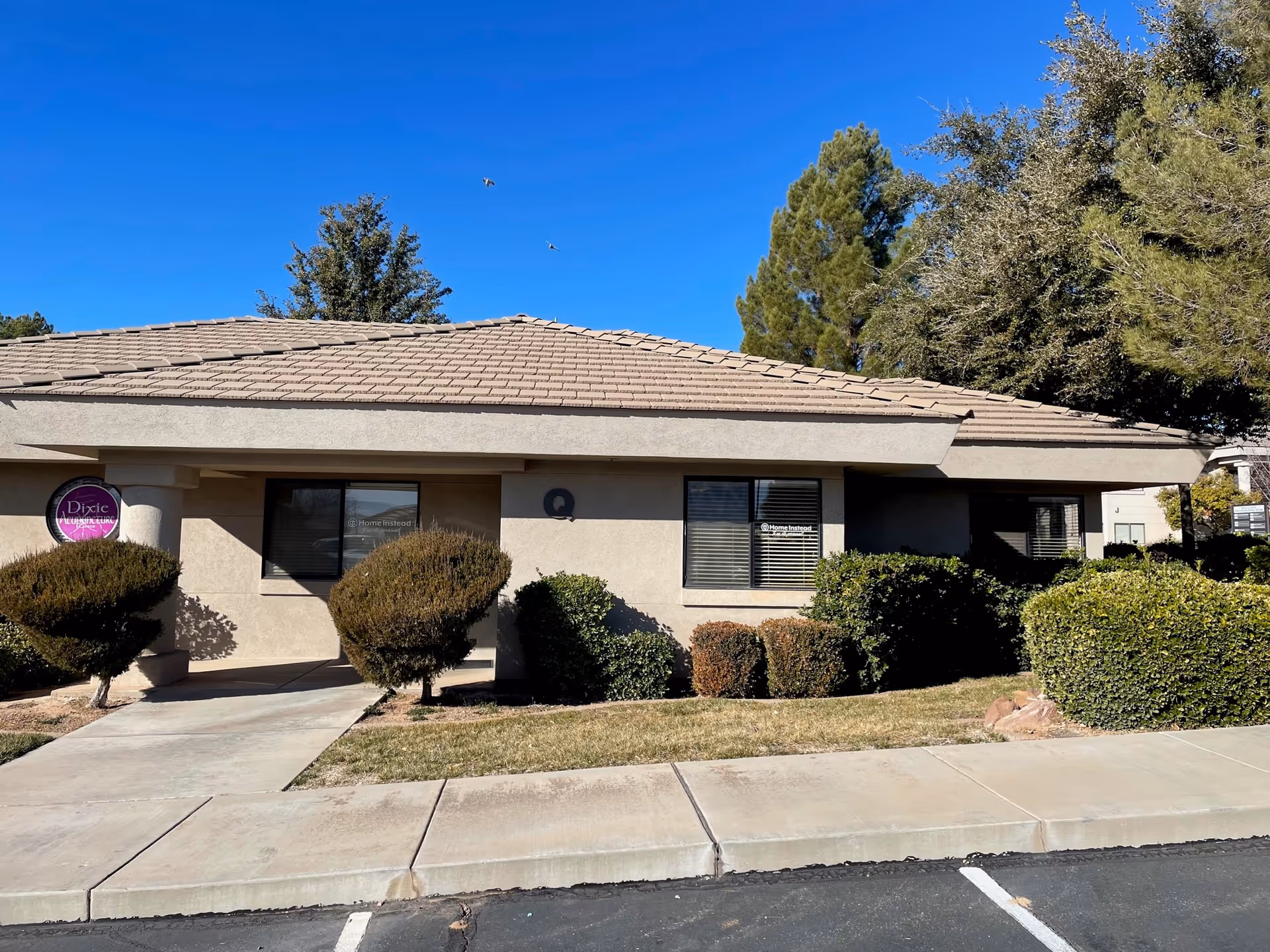 One-story beige building labeled Home Instead, with a tiled roof and surrounding shrubs.