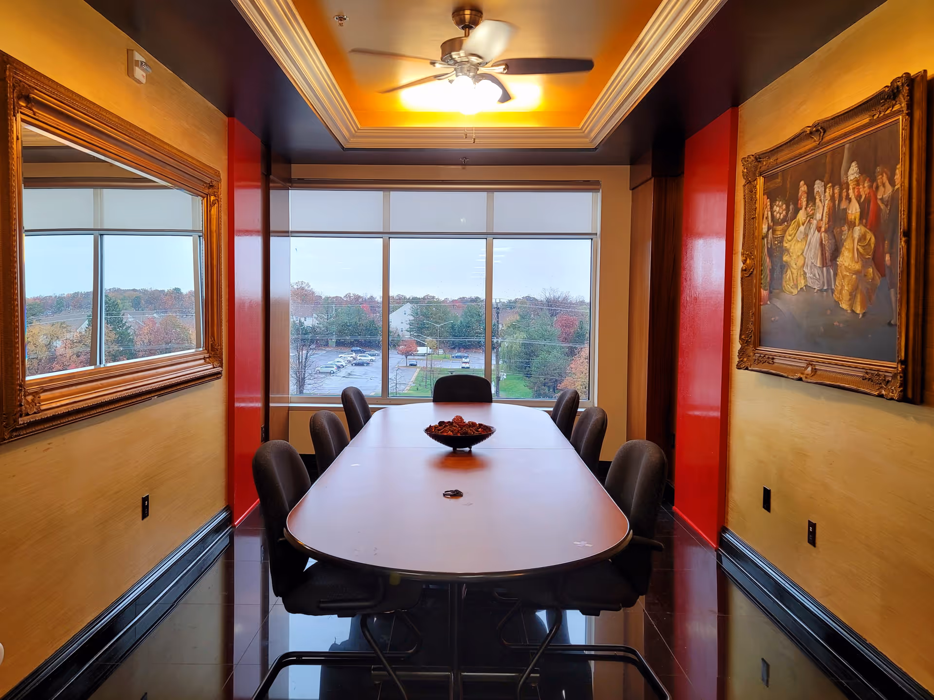 A long dining table with chairs in a warmly lit interior near a large window.