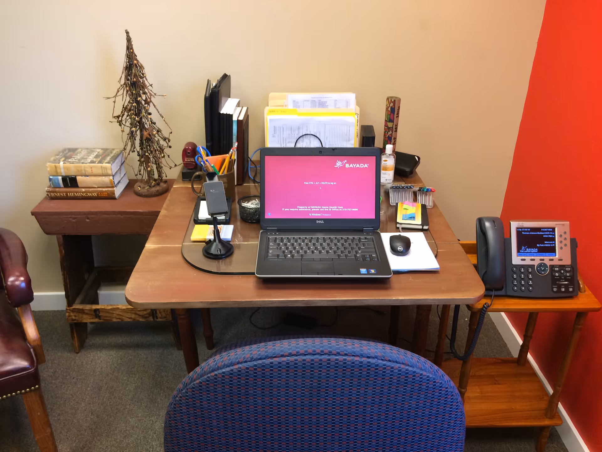 A wooden desk with laptop, phone, and office supplies in a Bayada Hospice workspace.