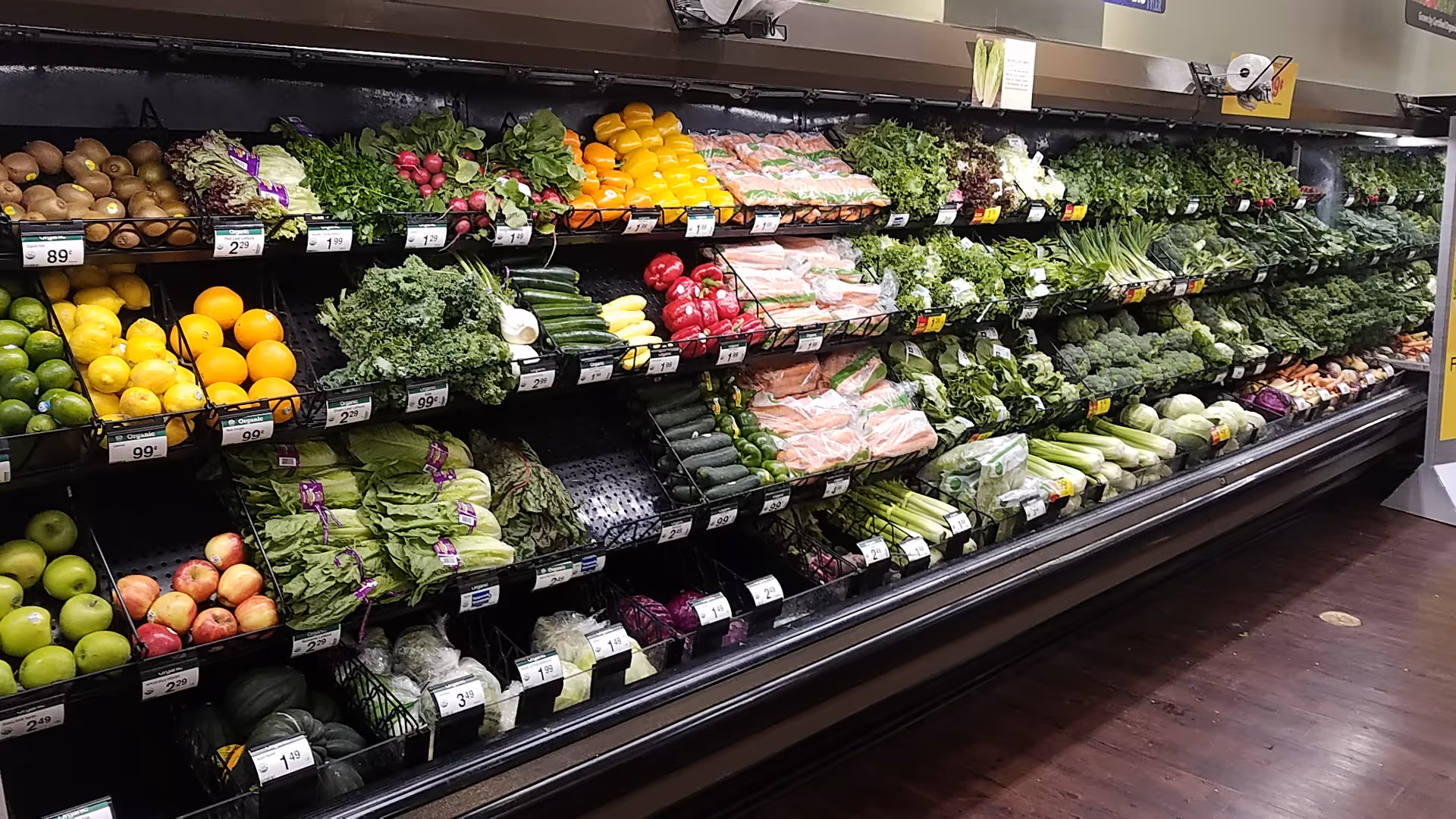 A vibrant grocery produce section with greens, fruits, and vegetables on shelves.