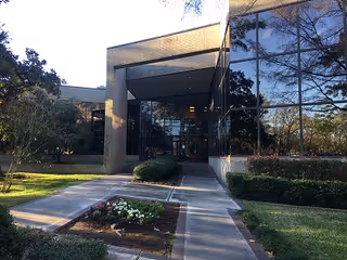 Modern glass-front building entrance with a walkway and manicured landscaping.